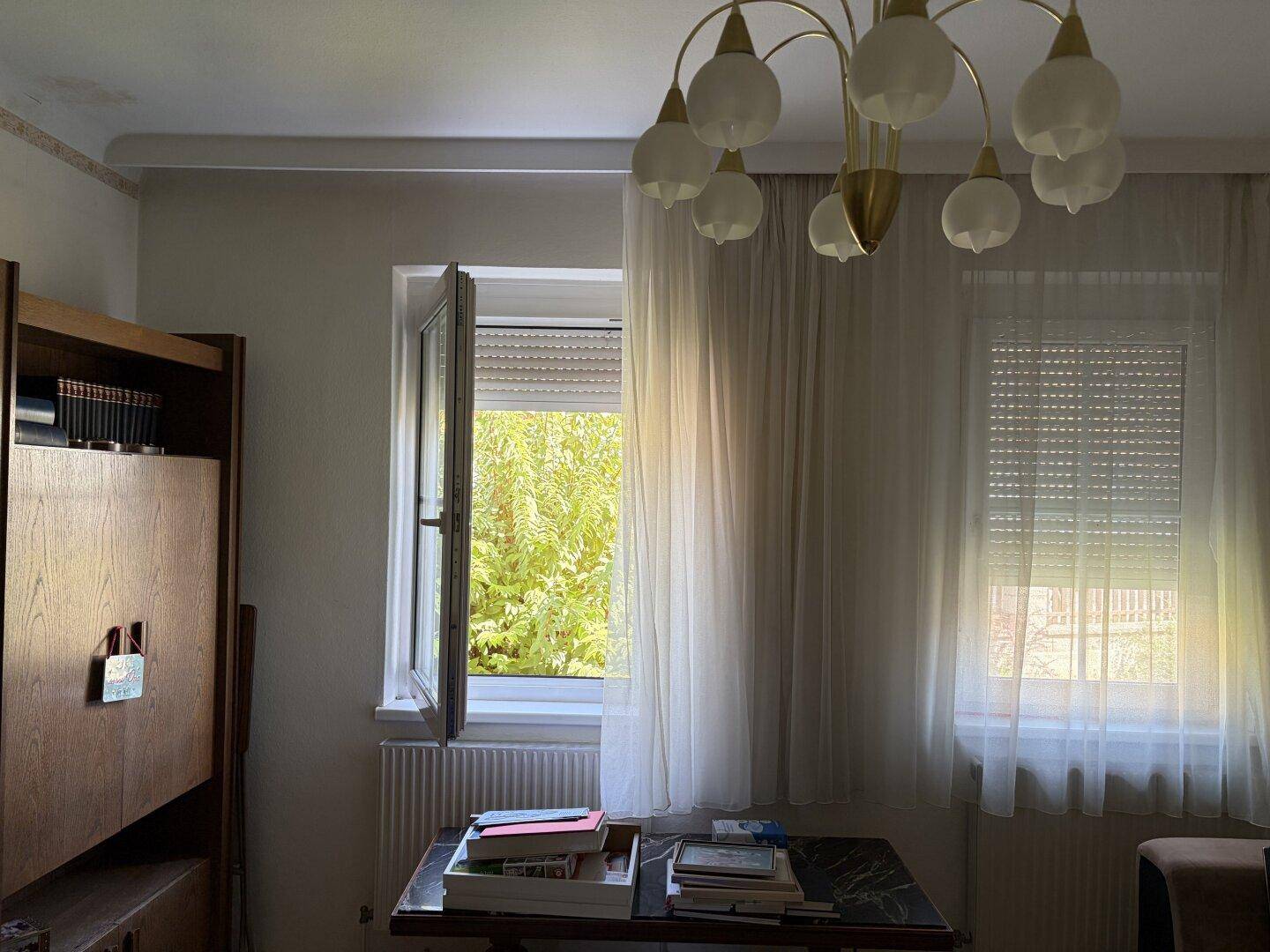 Wohnzimmer mit Vorhängen, einem Fenster mit Rollladen und einem Kronleuchter.