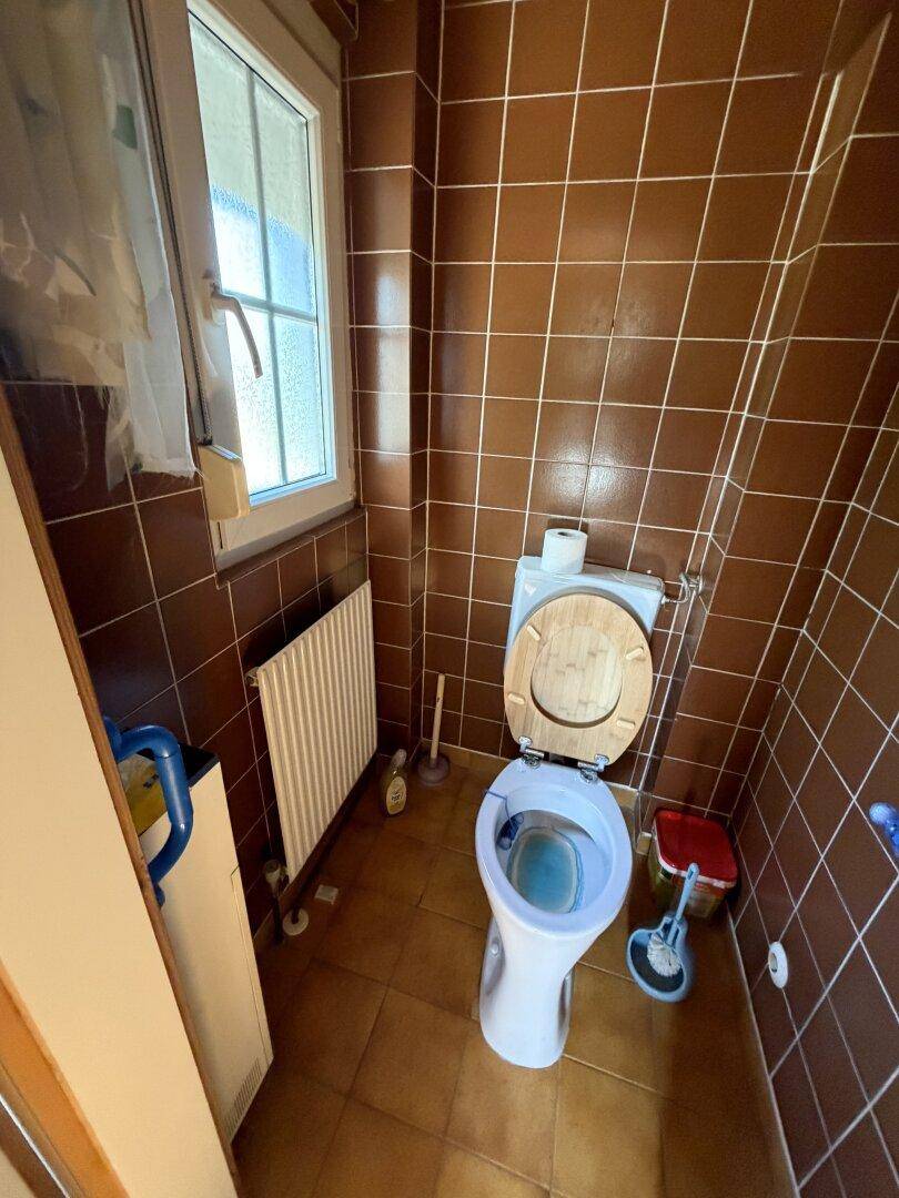 Kleines WC mit braunen Fliesen, Fenster und Heizkörper, einfach ausgestattet.