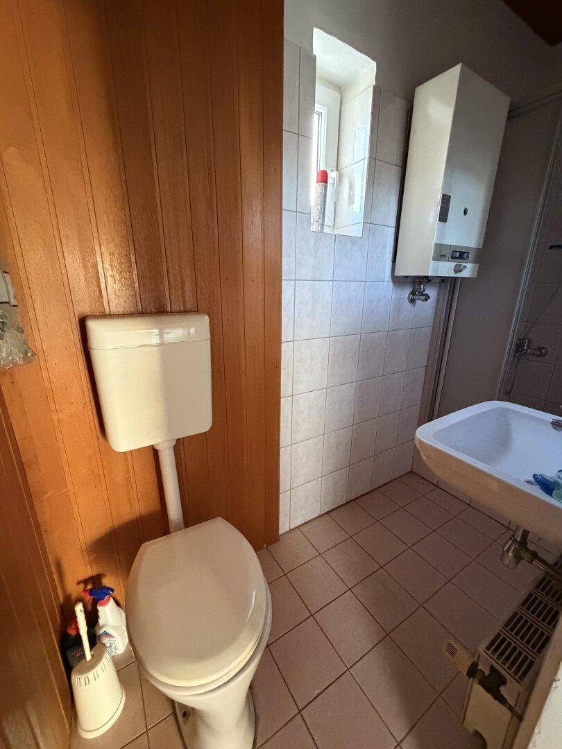 Badezimmer mit WC, Waschbecken, hellen Fliesen und Holzverkleidung an den Wänden.