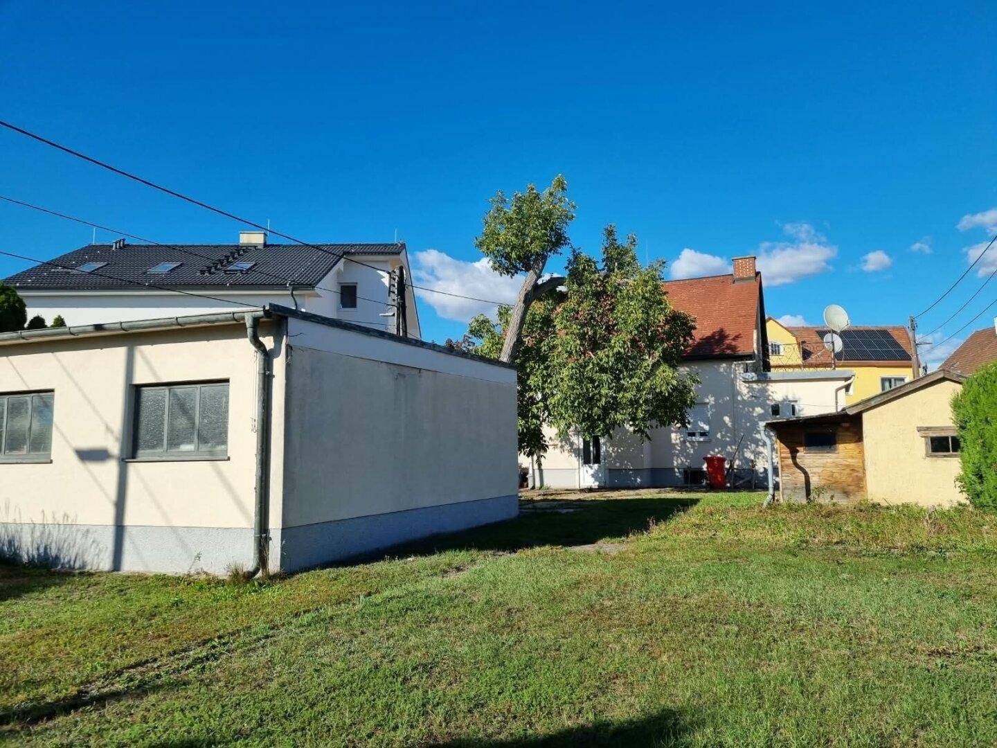 Weitläufige Rasenfläche im Garten mit Blick auf benachbarte Häuser und einen Schuppen.