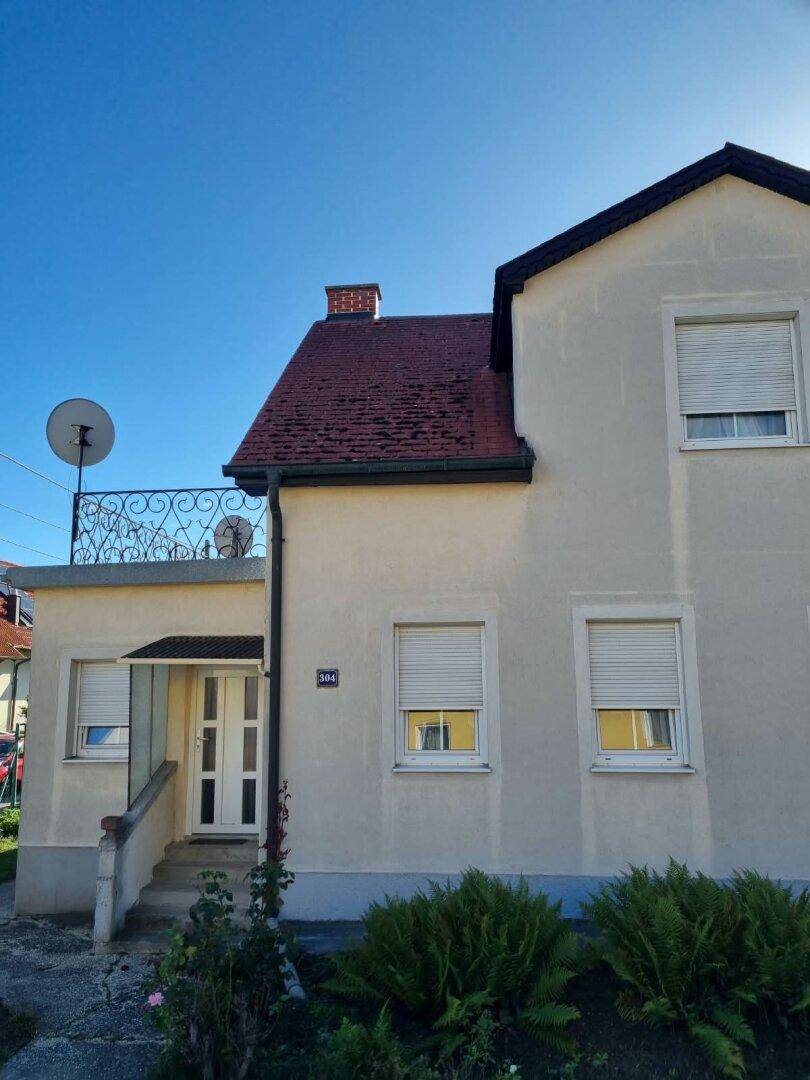 Vorderansicht des Hauses mit Eingang, Balkon und Rollläden, umgeben von gepflegten Sträuchern.
