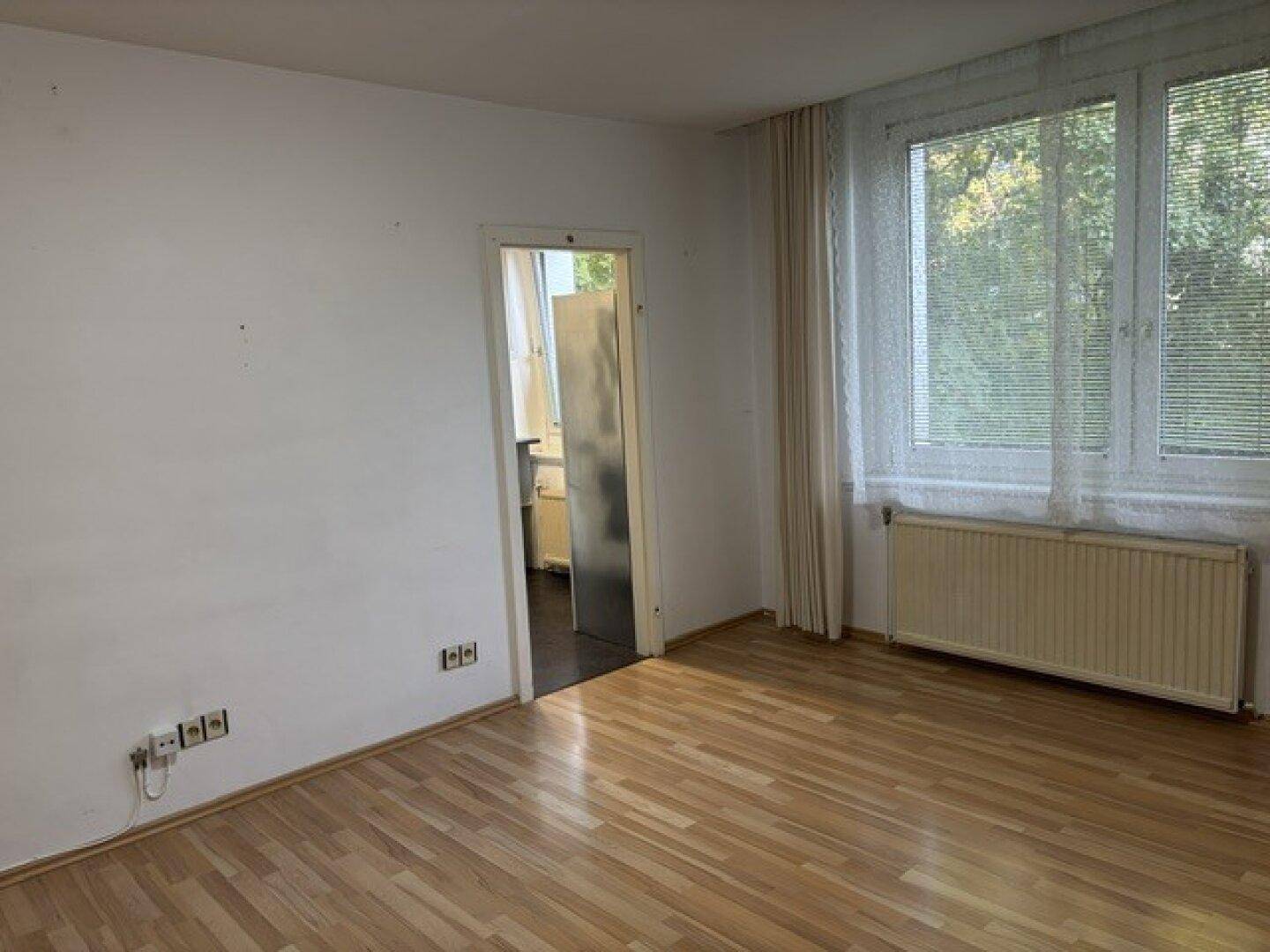 Helles, unmöbliertes Zimmer mit Laminatboden und großen Fenstern, die viel Tageslicht hereinlassen.