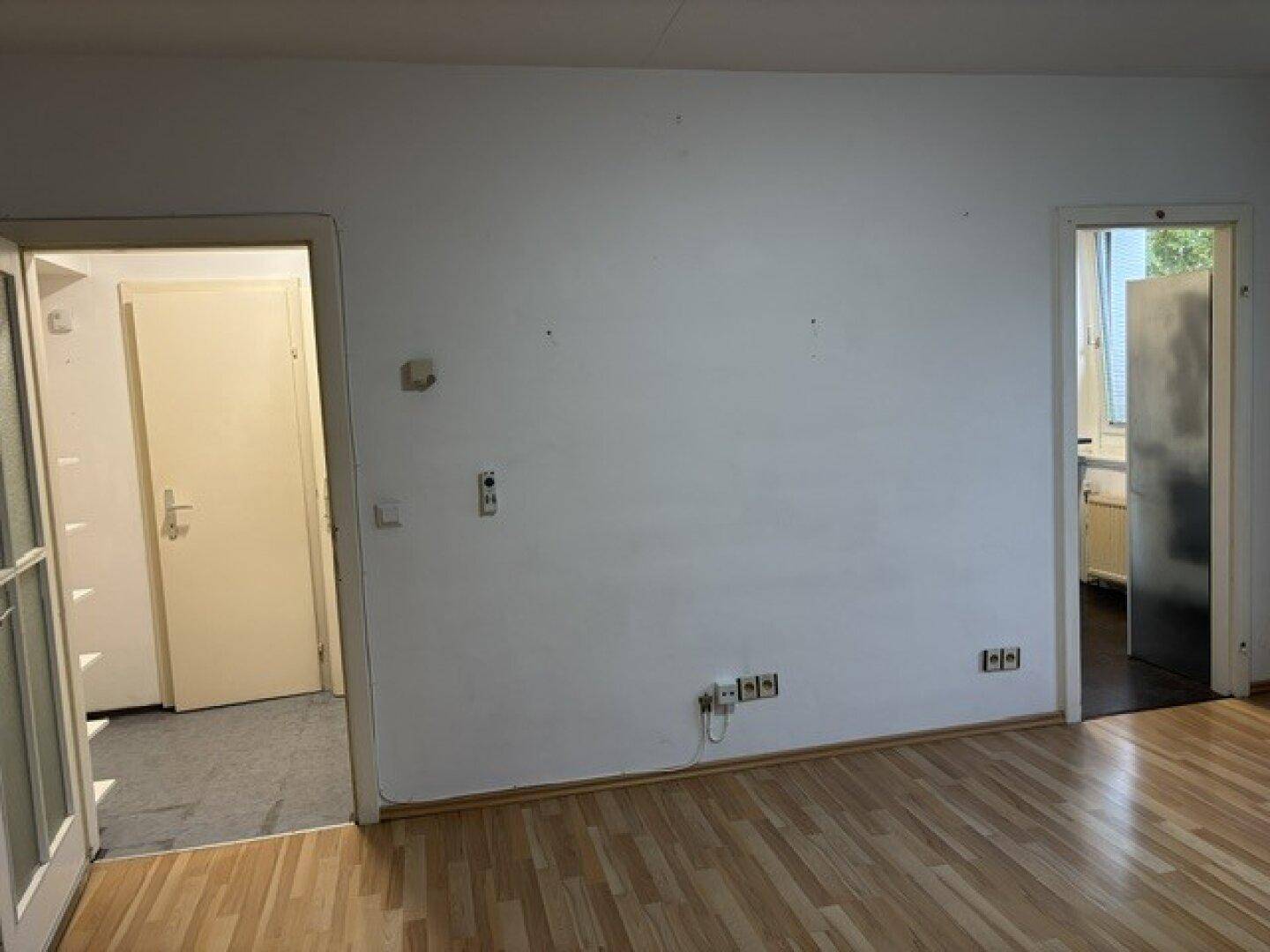 Geräumiges, leeres Zimmer mit Laminatboden und zwei Türöffnungen, bereit zur individuellen Gestaltung.