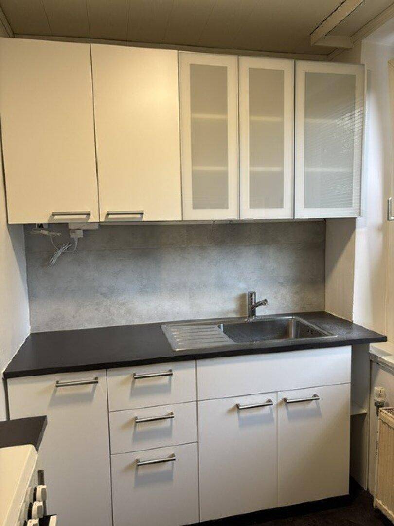 Kleine, moderne Küche mit weißen Schränken, dunkler Arbeitsplatte und integriertem Spülbecken.