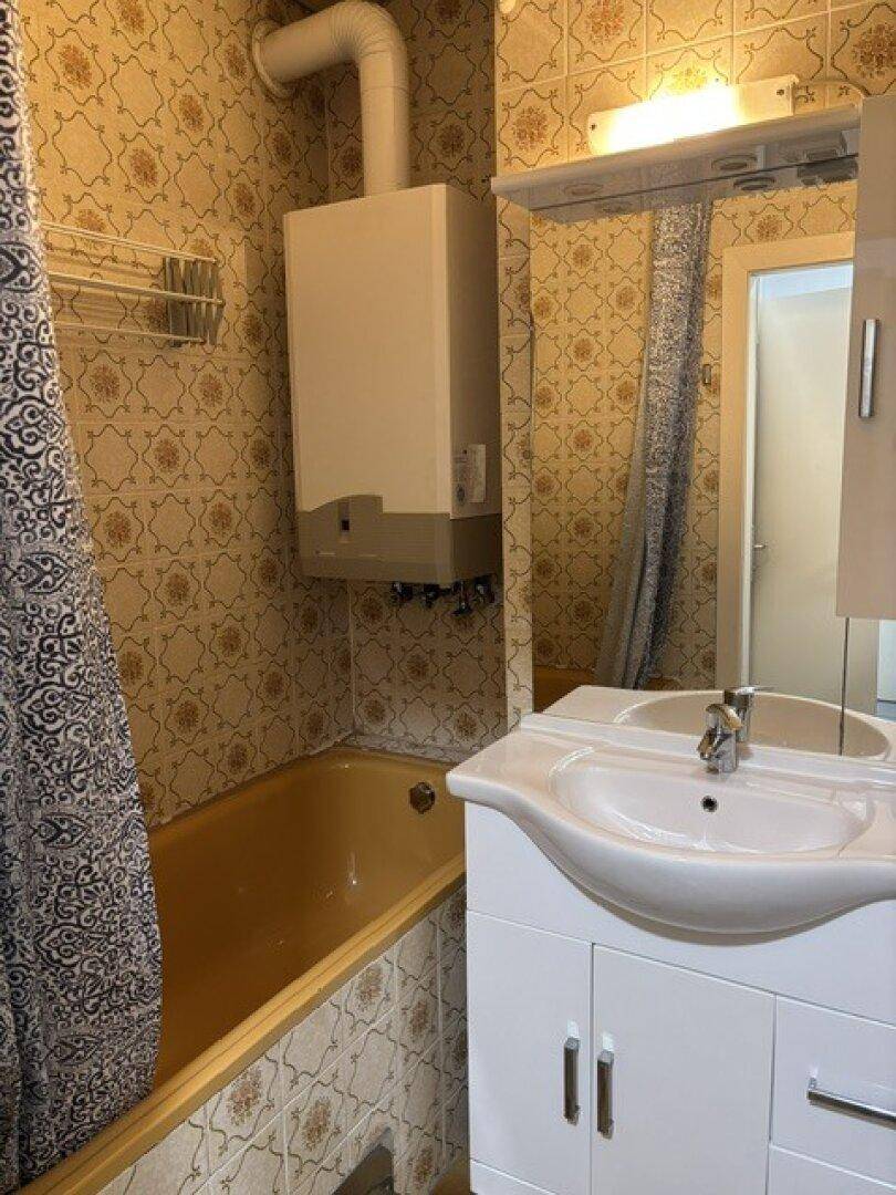 Badezimmer im 80er-Jahre-Stil mit Badewanne, Waschbecken und gemusterten Fliesen, inklusive Boiler.