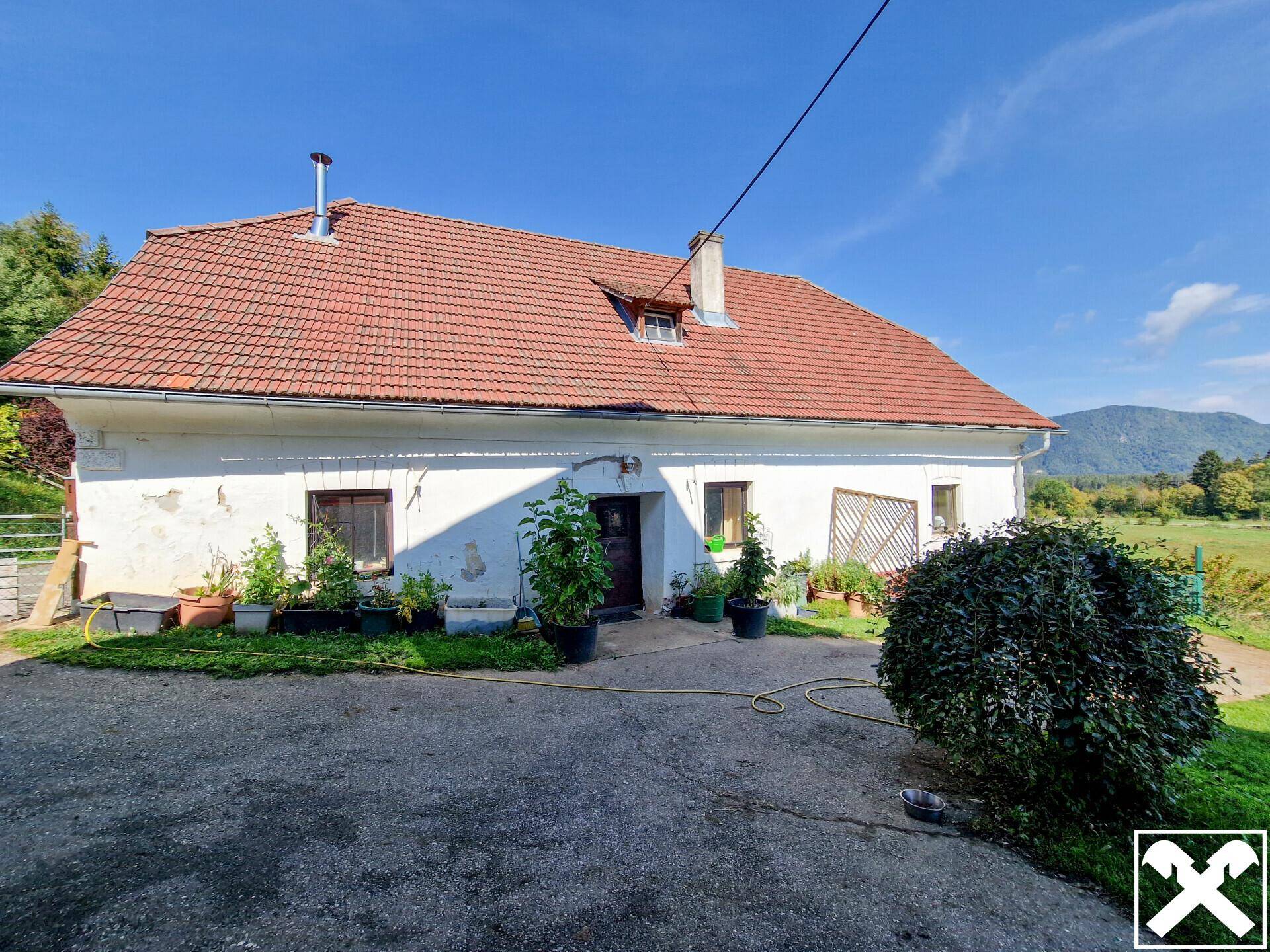 Älteres Landhaus mit weiß getünchter Fassade, rotem Ziegeldach und grüner Umgebung.