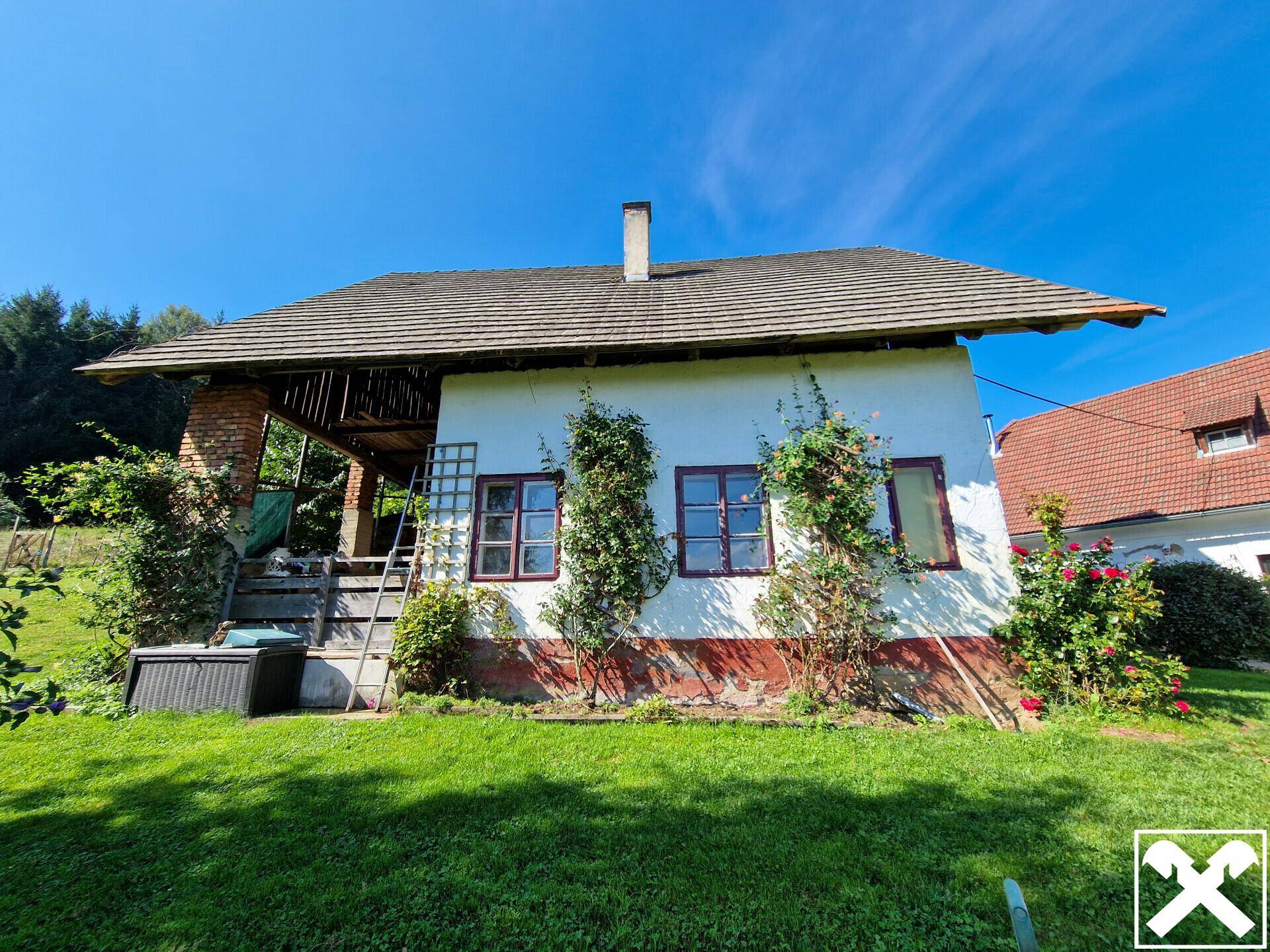 Rustikales Bauernhaus mit überdachtem Außenbereich und grüner Umgebung.