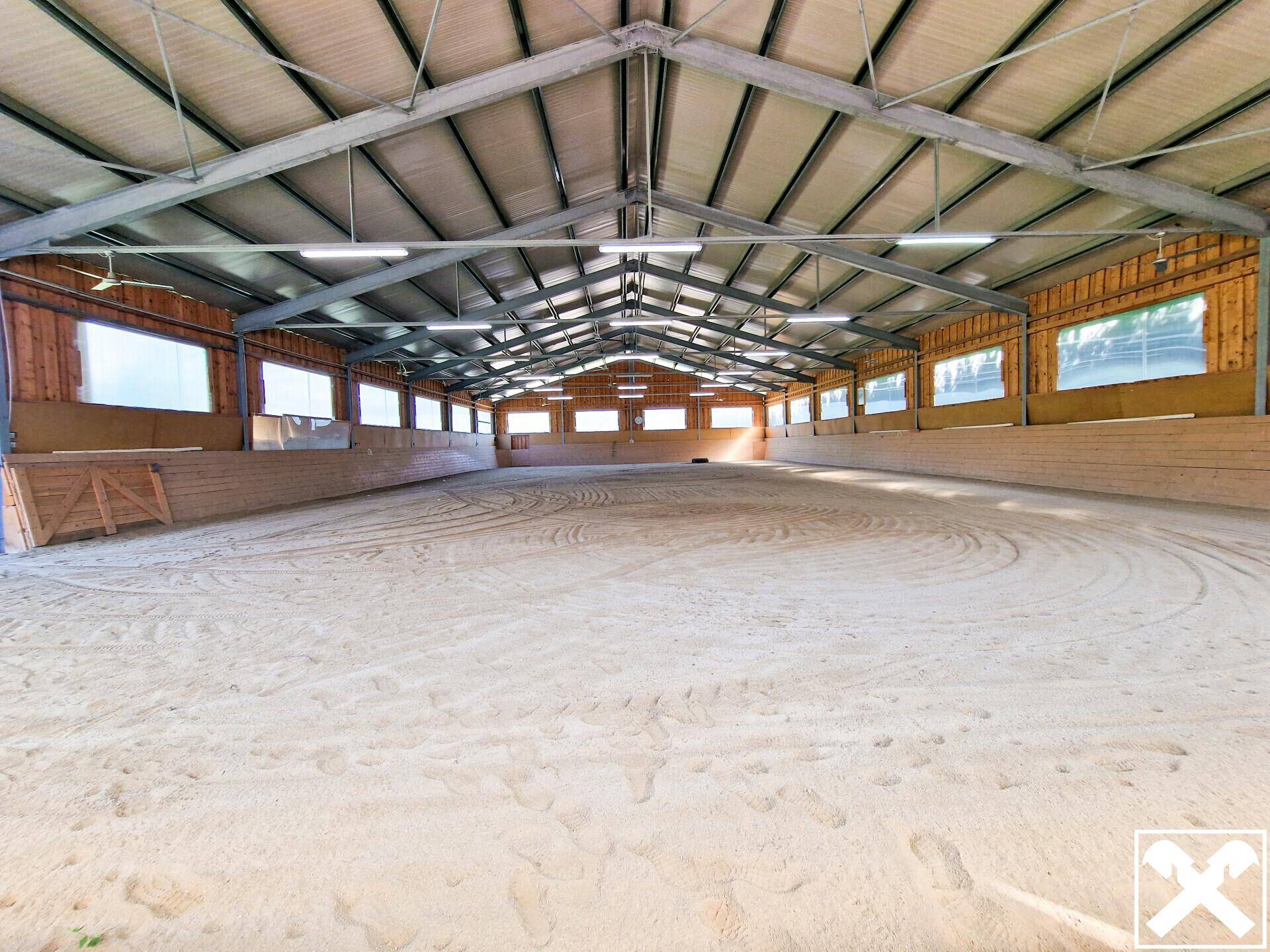 Große Reithalle mit Sandboden und Metallkonstruktion für Pferdesport.