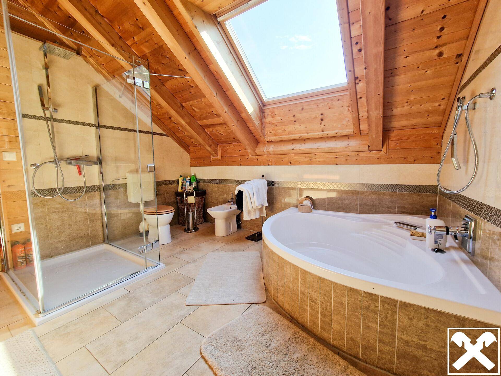 Geräumiges Badezimmer mit Eckbadewanne, Dusche, Dachfenster und Holzbalken.