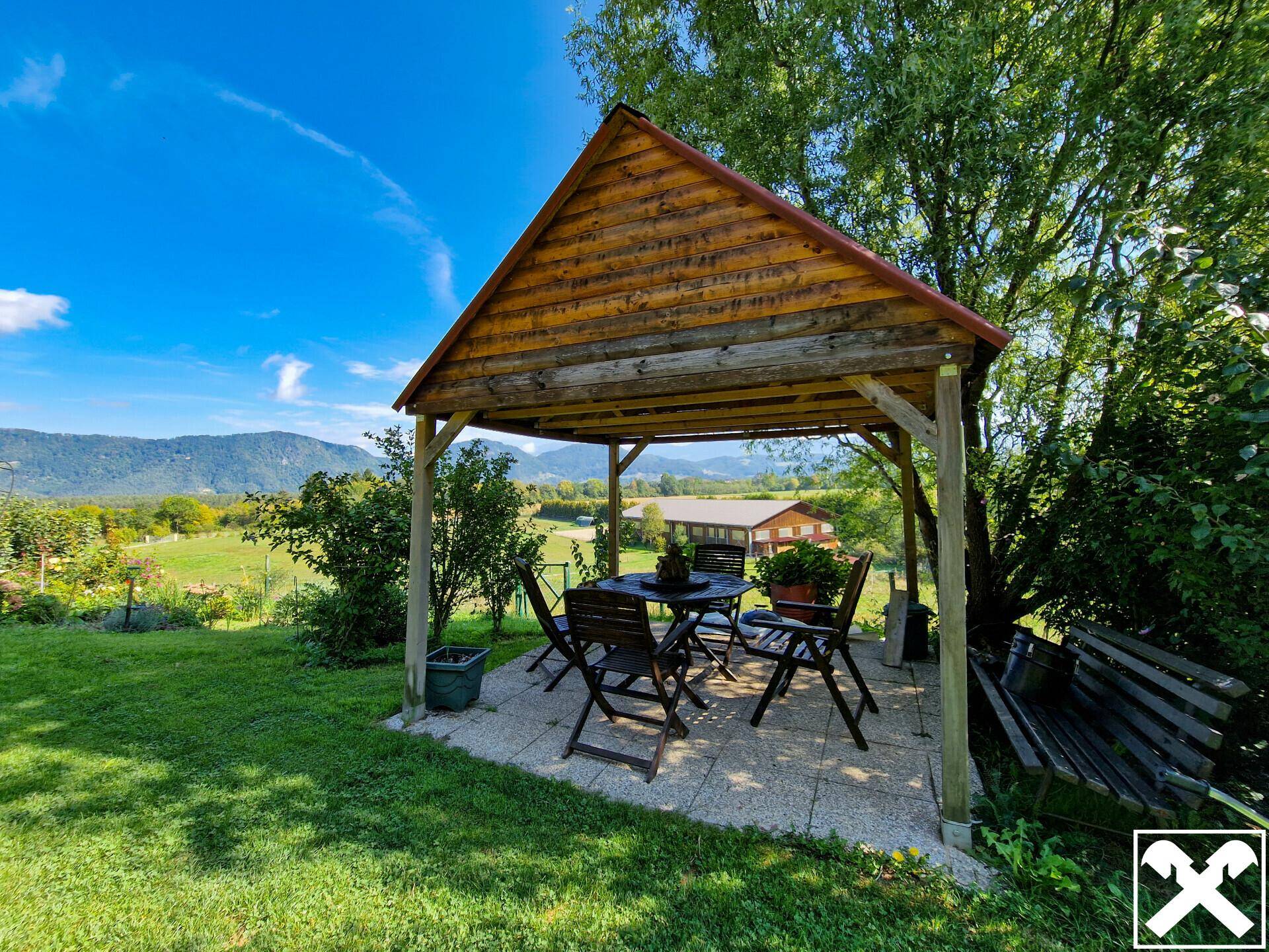 Gemütlicher Holzpavillon mit Sitzgelegenheiten im Garten und Bergblick.