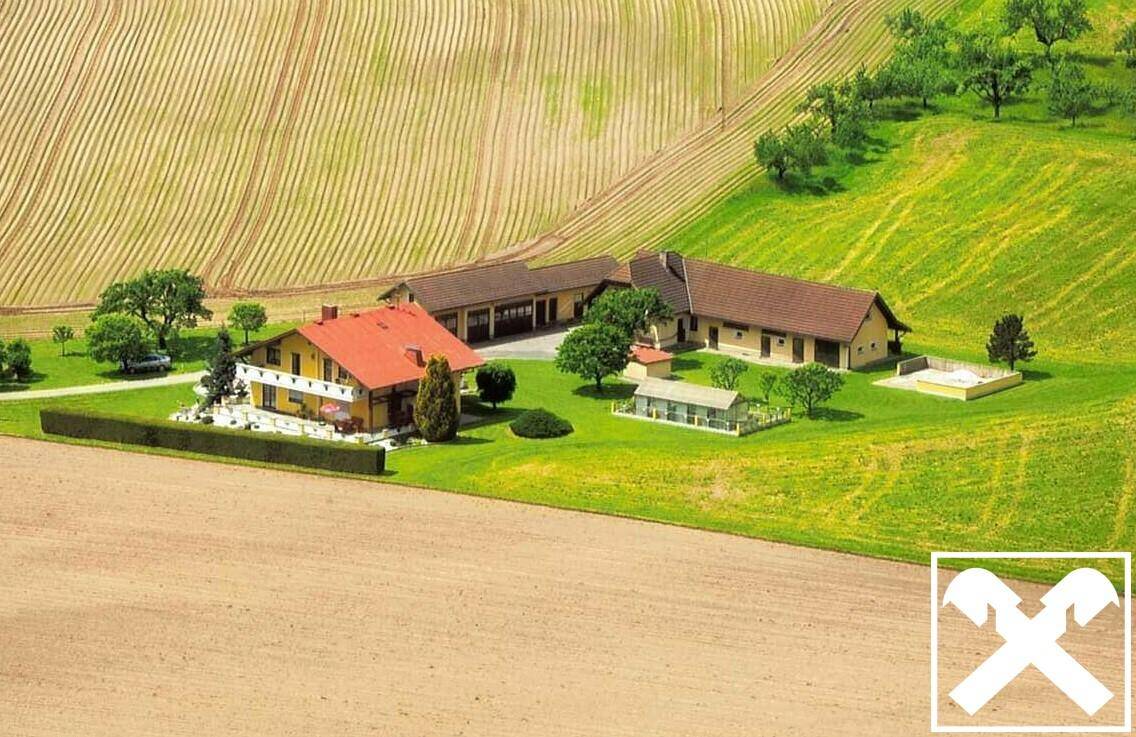 Luftaufnahme des Anwesens mit mehreren Gebäuden, umgeben von Feldern und grünen Hügeln.