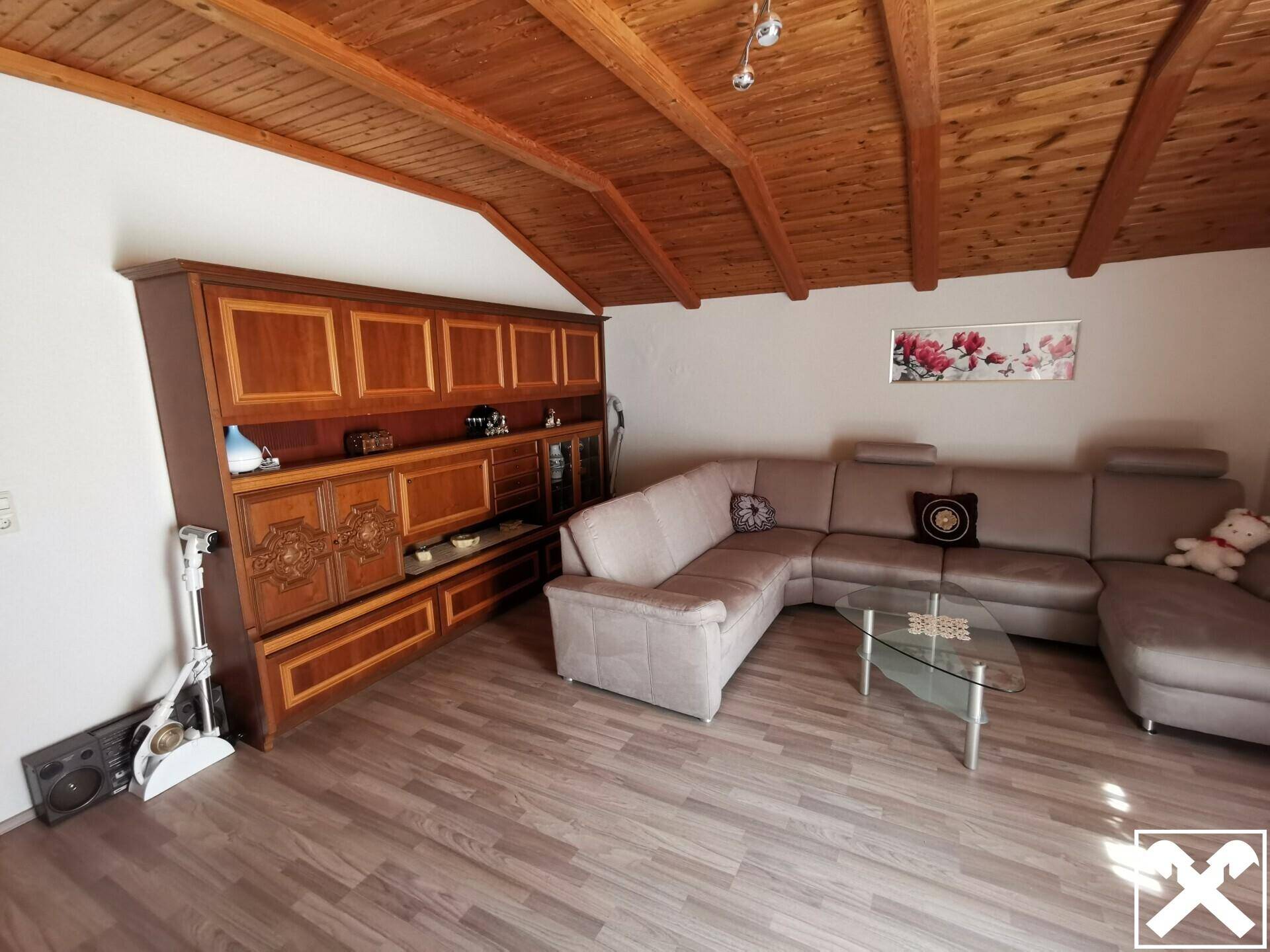 Gemütliches Wohnzimmer im Dachgeschoss mit Holzbalkendecke und großem Sofa.