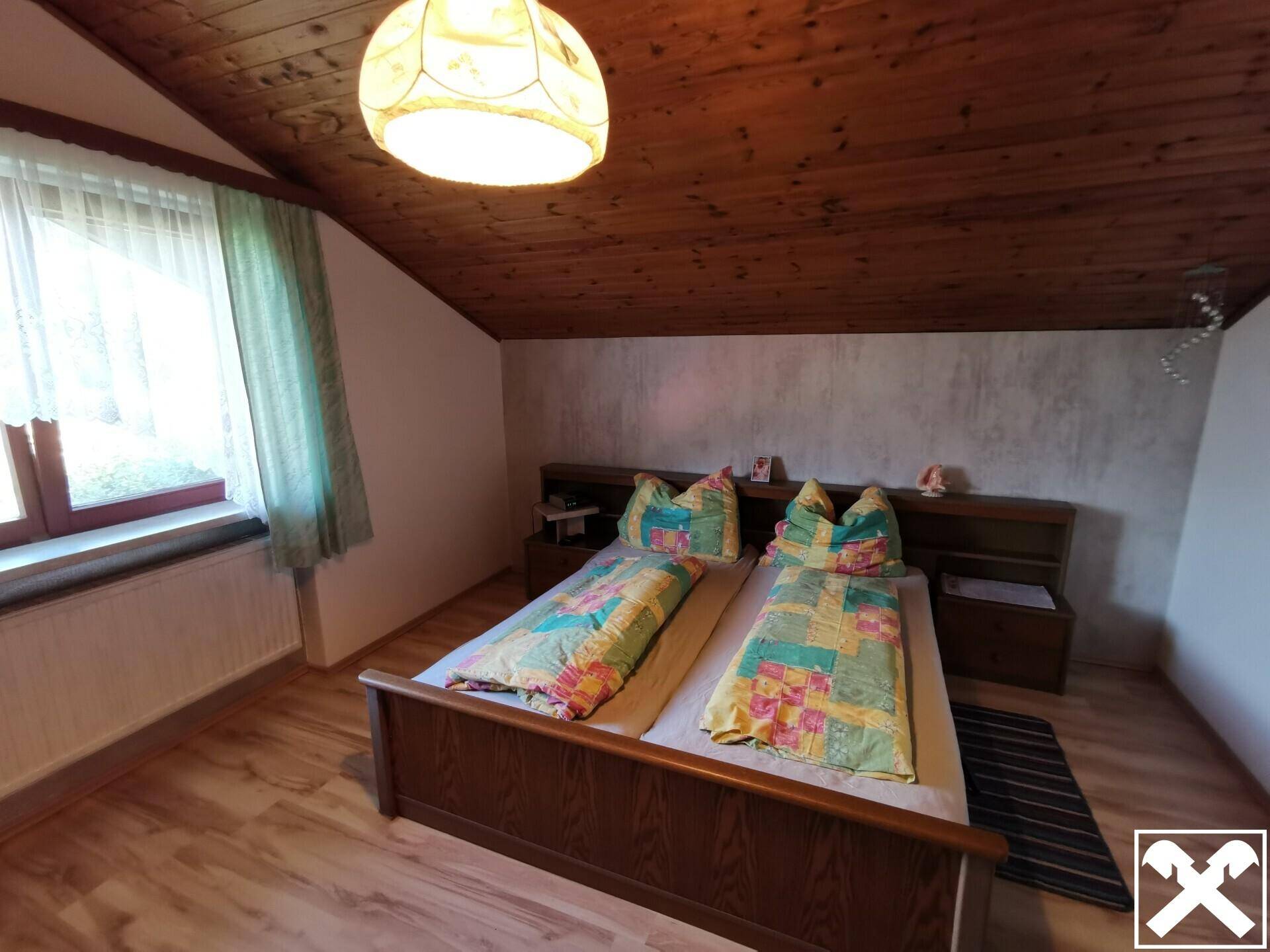 Schlafzimmer im Dachgeschoss mit Doppelbett, Holzbalkendecke und Fenster.