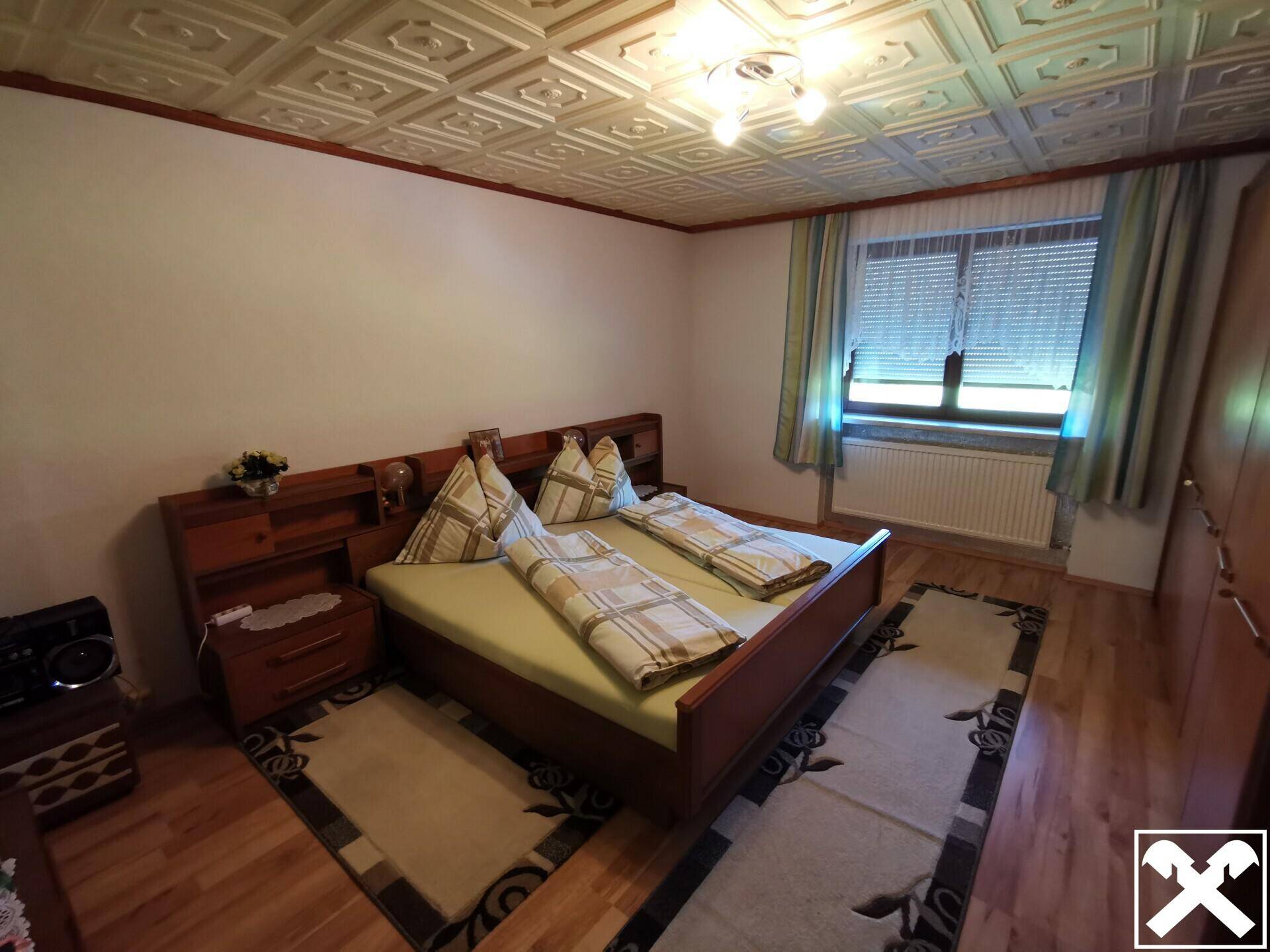 Schlafzimmer mit Doppelbett, Holzmöbeln und dekorativer Deckenverkleidung.