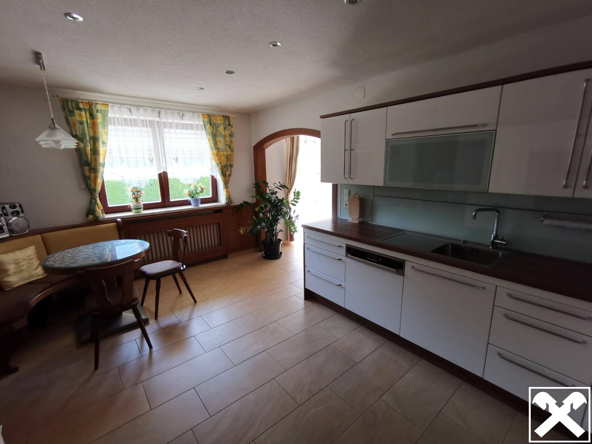 Helle Küche mit modernen weißen Schränken, Essbereich und Fliesenboden.