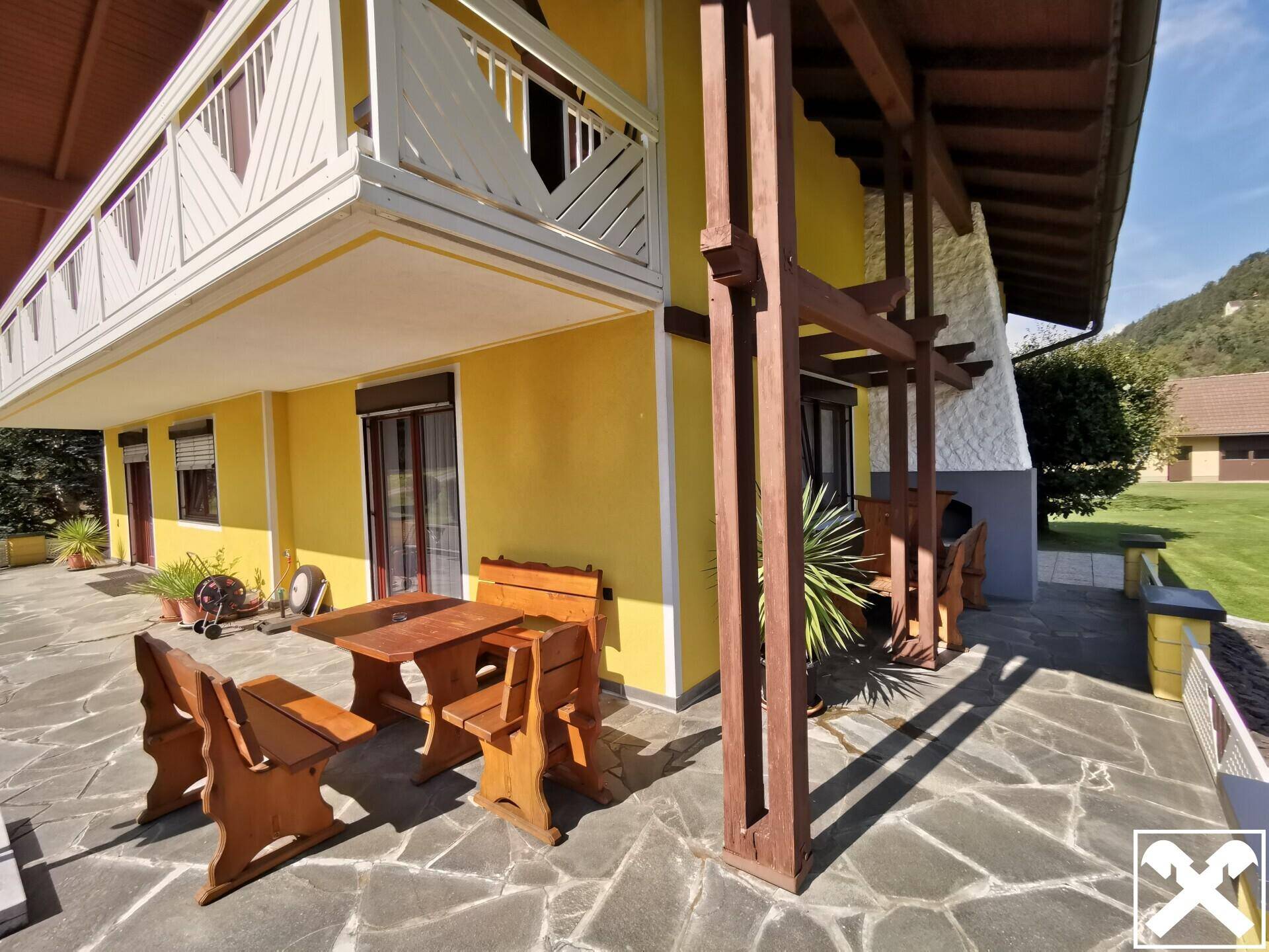 Gemütliche Steinterrasse mit rustikalen Holzmöbeln und Zugang zum Garten.