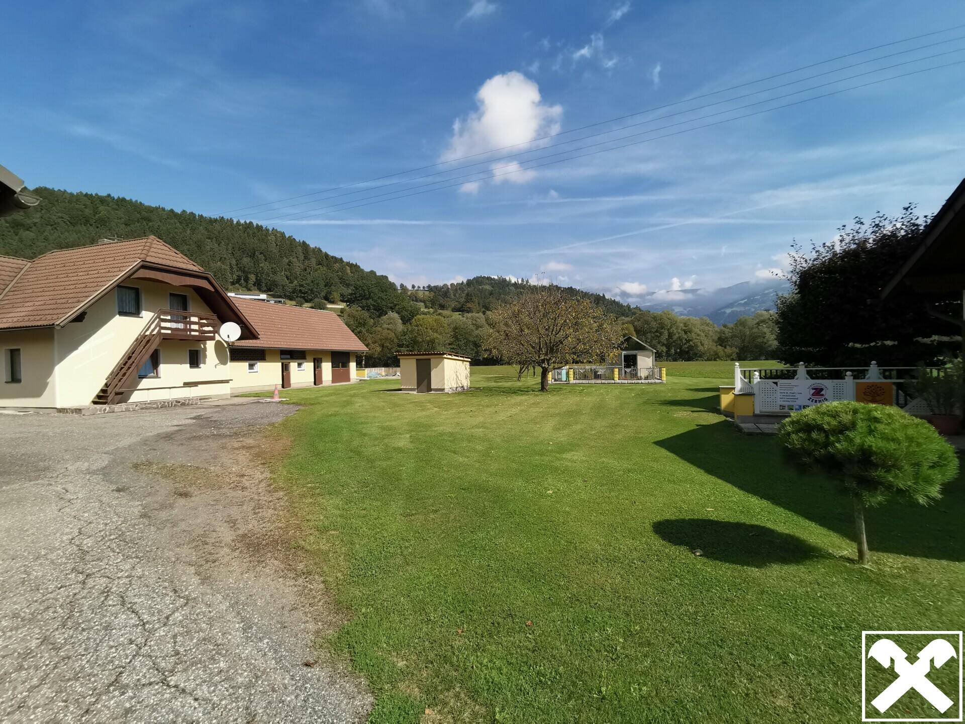 Großzügige Rasenfläche mit Blick auf die Gebäude und die umliegende Berglandschaft.