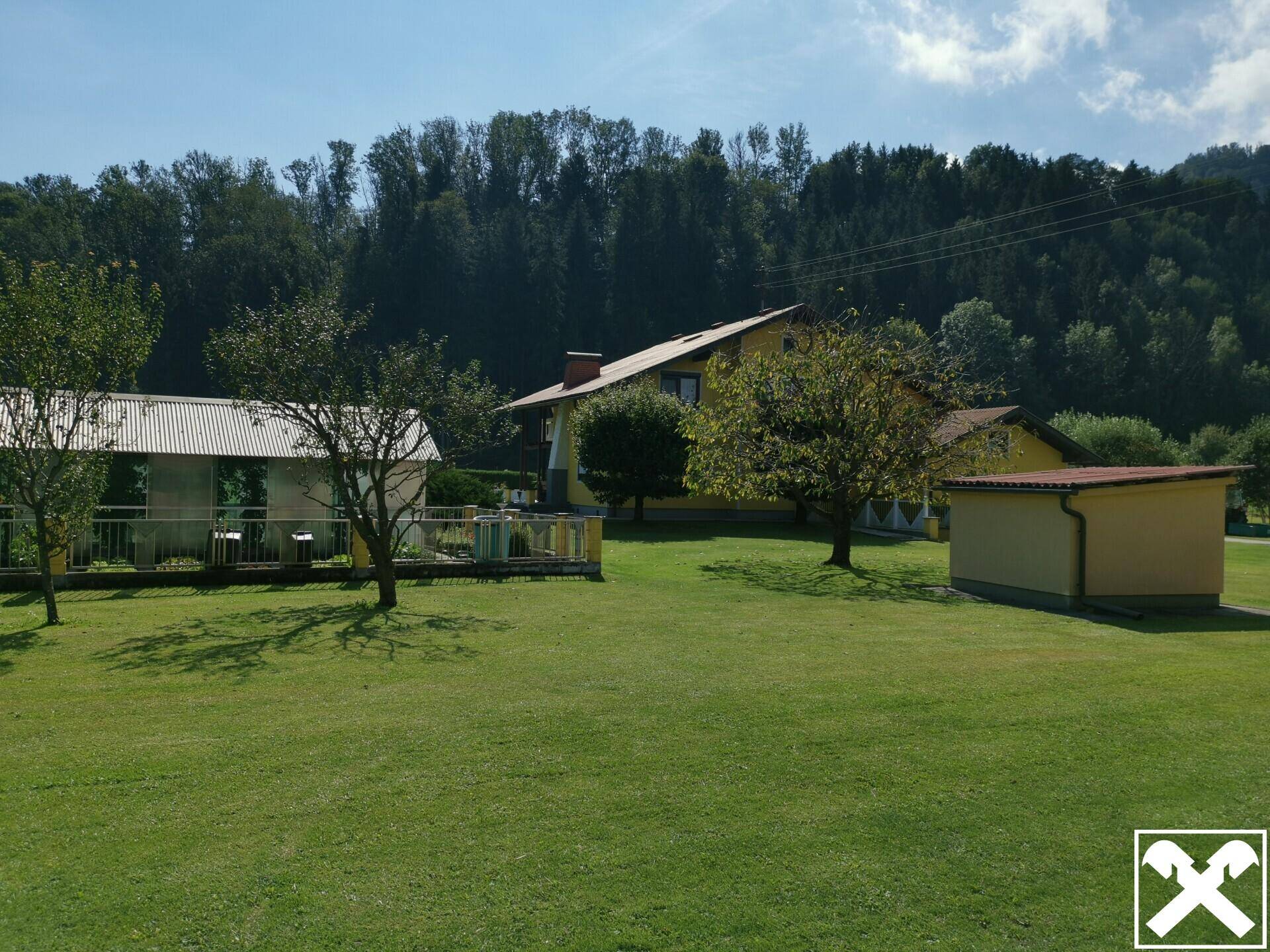 Weitläufiger grüner Gartenbereich mit Bäumen und Blick auf die umliegende Naturlandschaft.