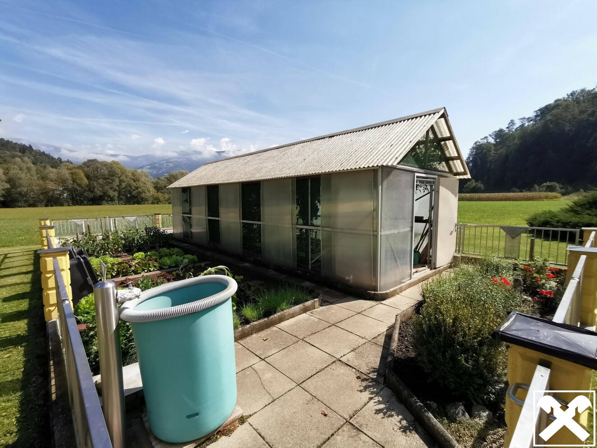 Gewächshaus und gepflegter Gemüsegarten mit Blick auf die ländliche Umgebung.