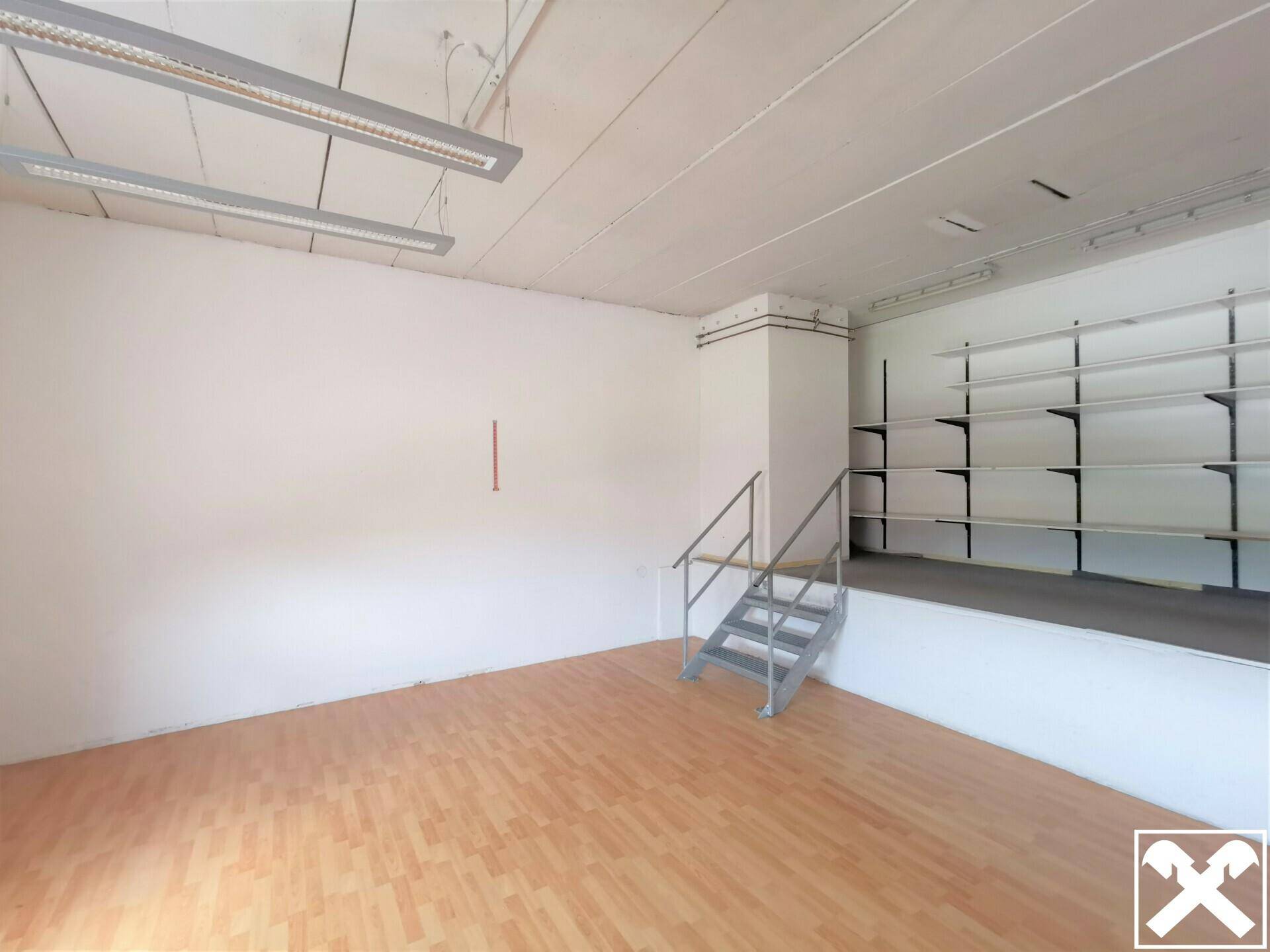 Geräumiger Verkaufsraum mit Holzboden, Regalen und einer kleinen erhöhten Plattform mit Treppe.