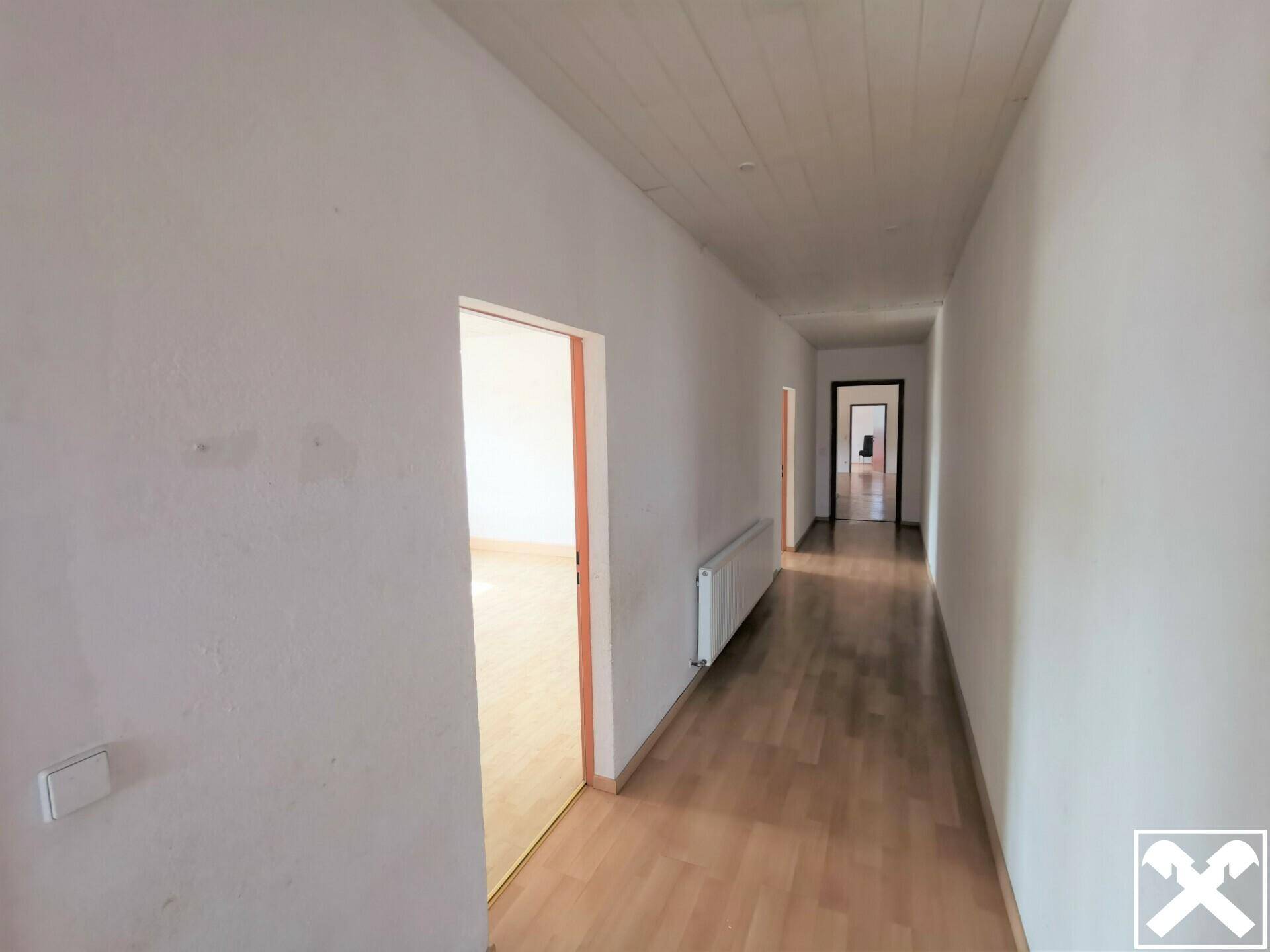 Langer, heller Flur mit Holzboden und mehreren Türen, der verschiedene Räume in der Immobilie verbindet.