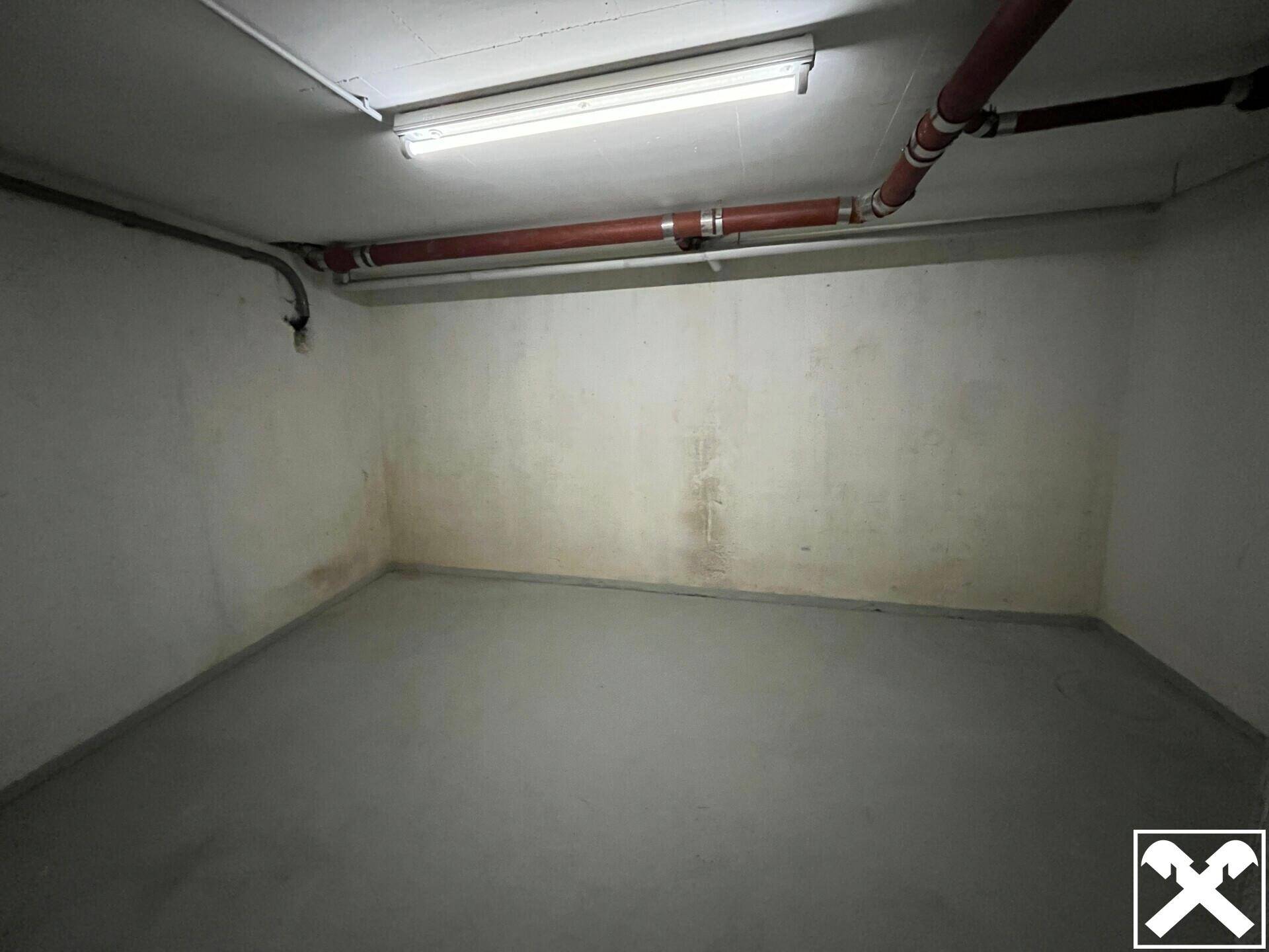 Einfacher Kellerraum mit Betonboden und Deckenbeleuchtung, geeignet für verschiedene Lagerzwecke.