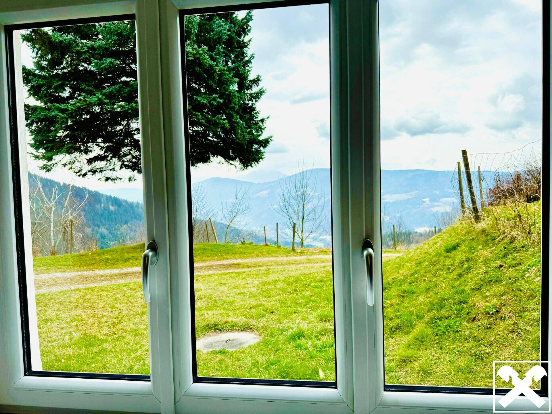 Fenster mit weitem Blick auf die grüne Hügellandschaft und die Berge in der Ferne.
