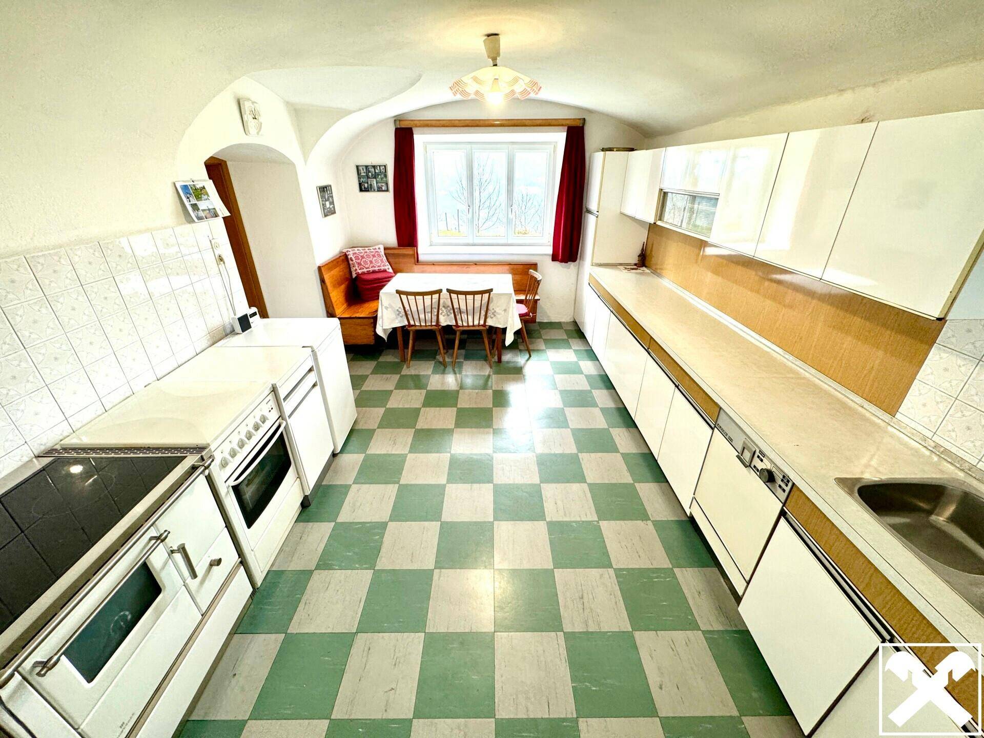Traditionelle Küche mit kariertem Boden, weißer Einbauküche und Essbereich am Fenster.