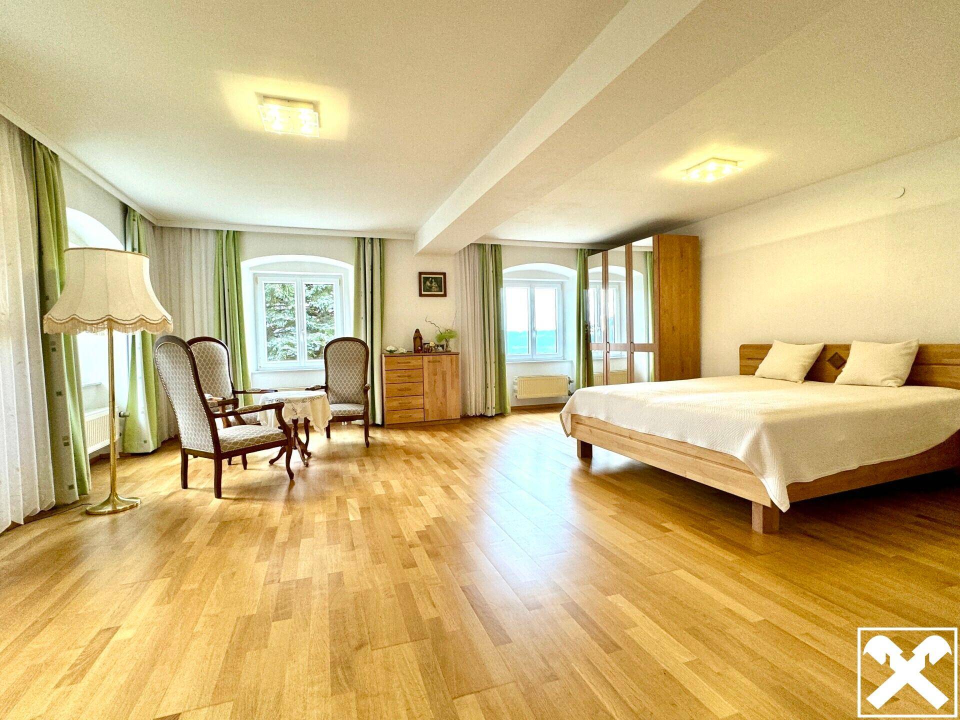Helles Schlafzimmer mit Holzboden, Doppelbett und Sitzbereich am Fenster.