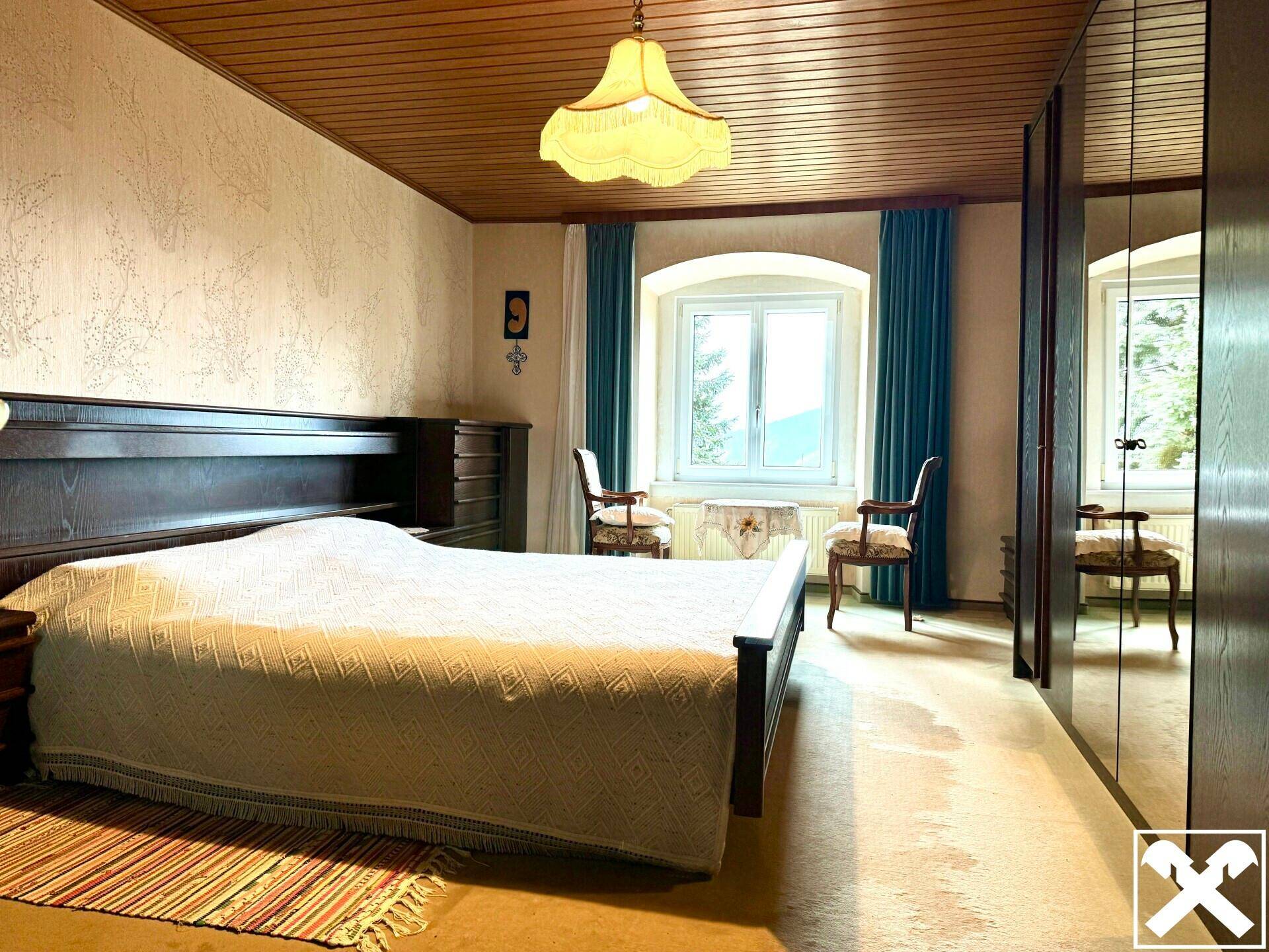 Schlafzimmer mit Holzbett, Holzdecke und Kleiderschrank, bietet Blick ins Grüne.
