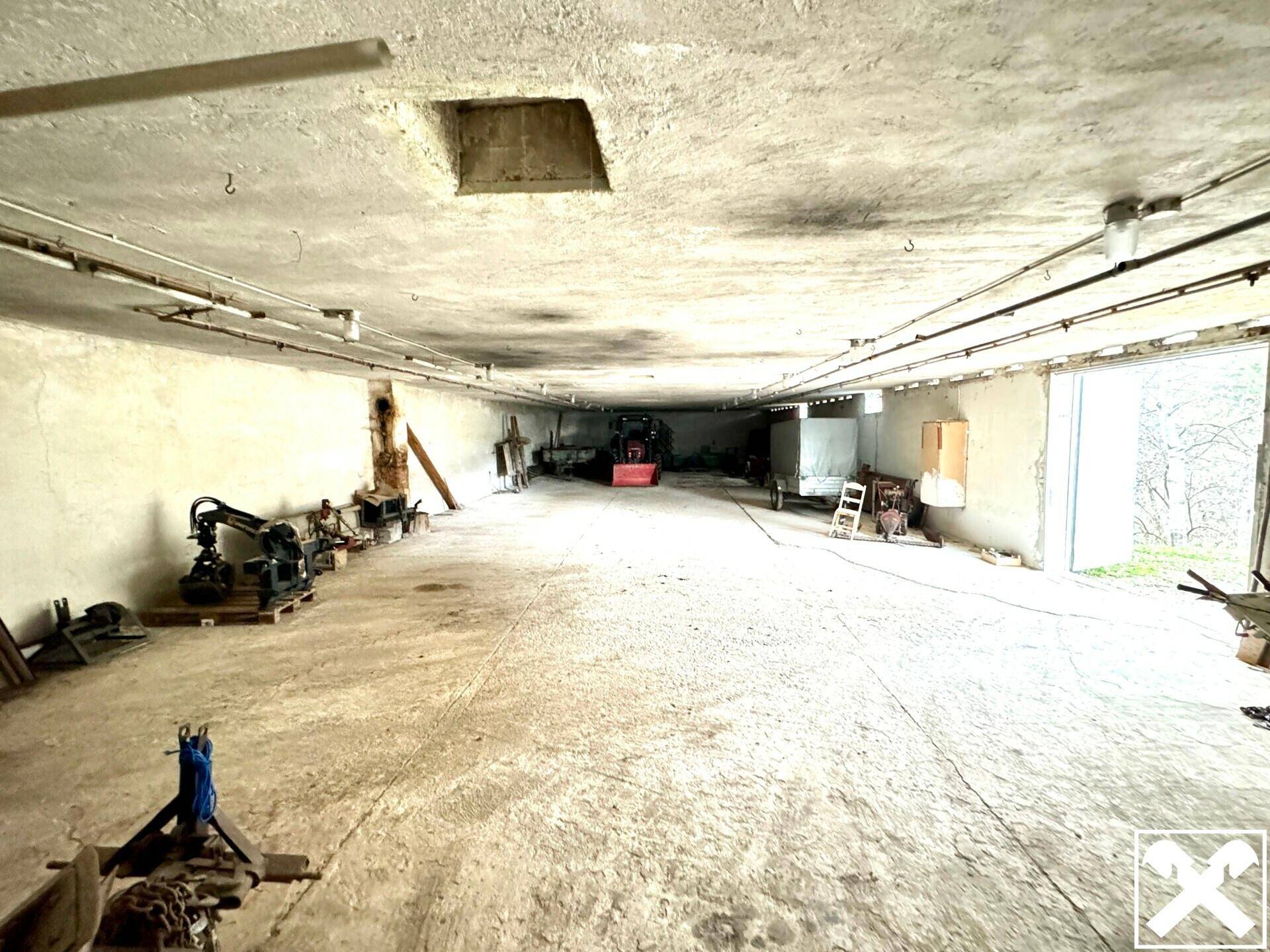 Großer, leerer Raum mit Betonboden und einigen Werkzeugen, ideal als Werkstatt oder Lagerbereich.