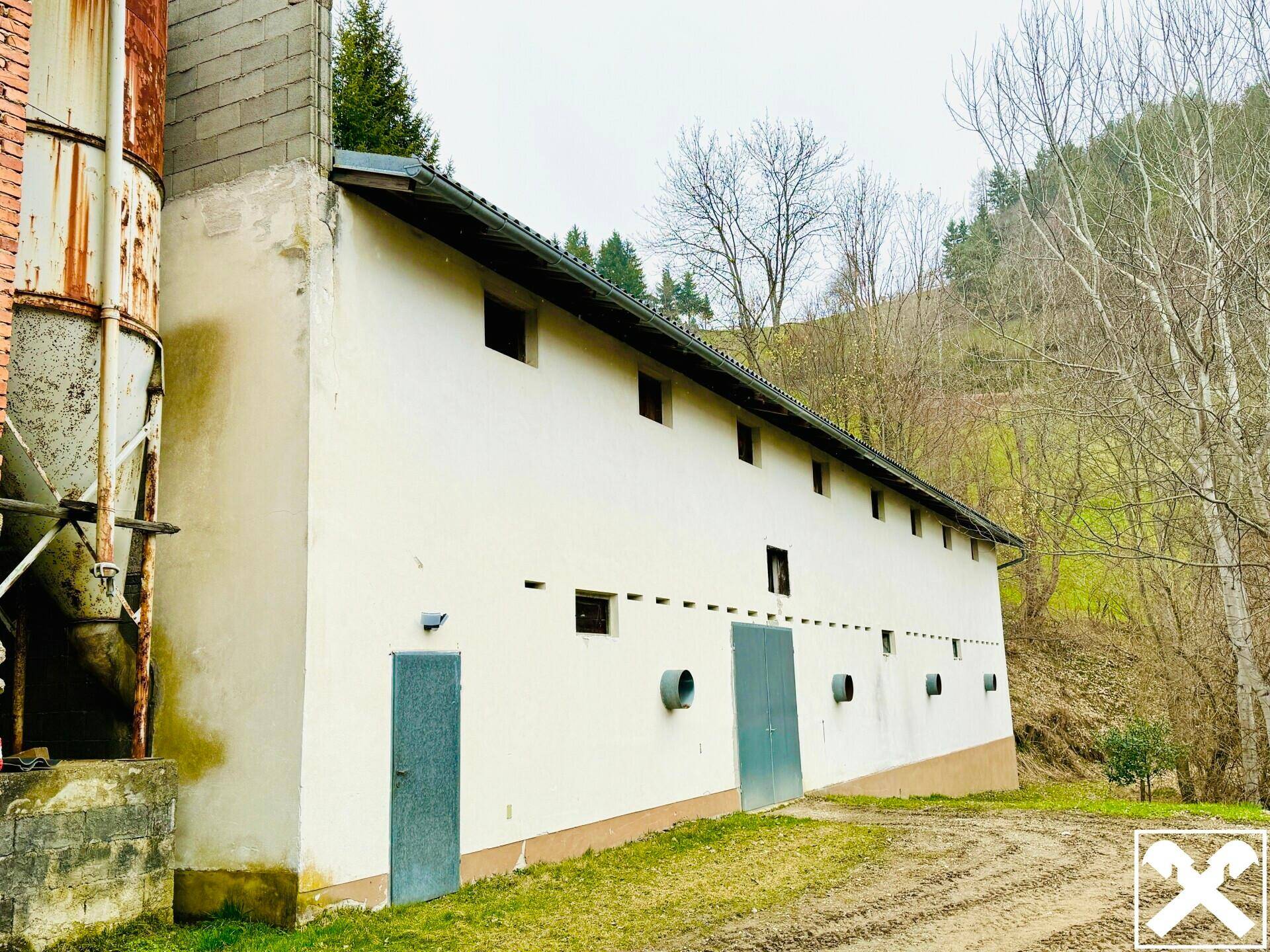 Langes, weißes Nebengebäude mit mehreren Türen und kleinen Fenstern, umgeben von ländlicher Natur.