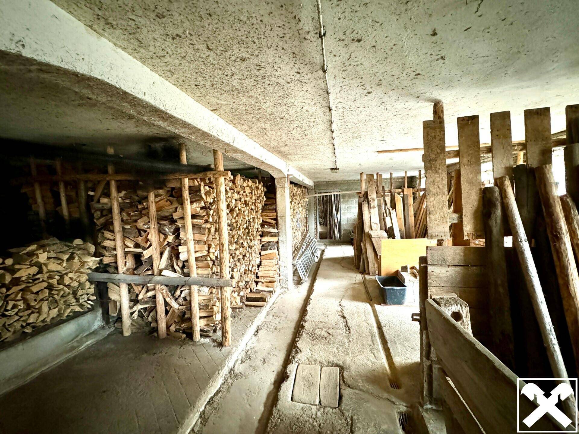 Kellerraum mit gestapeltem Brennholz und Holzbrettern, ideal als Lagerfläche für den Winter.