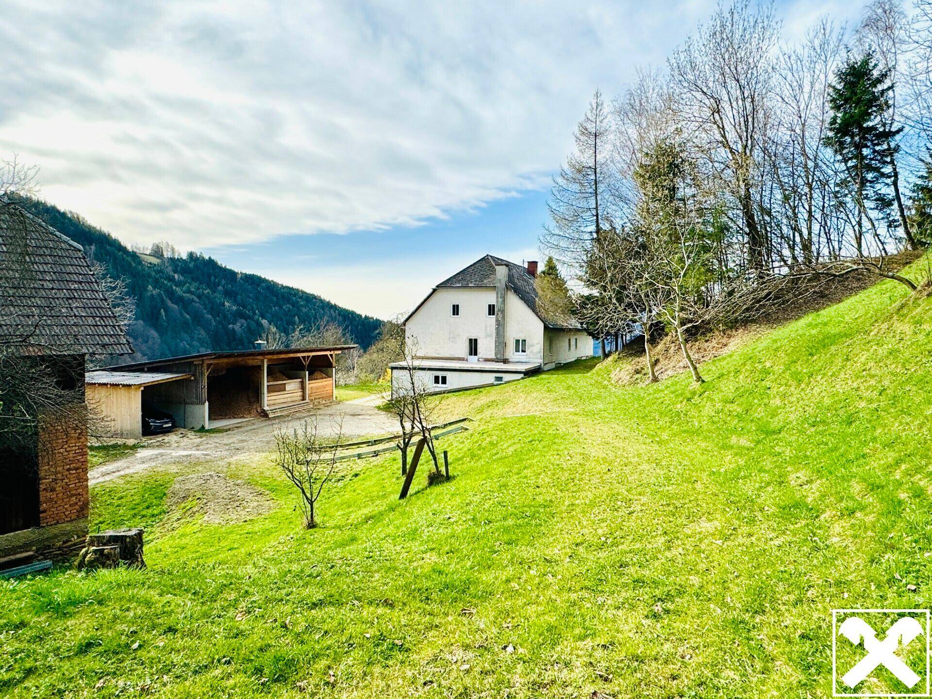 Ländliches Anwesen mit Haupthaus und Nebengebäuden, umgeben von grünen Wiesen und Bäumen.