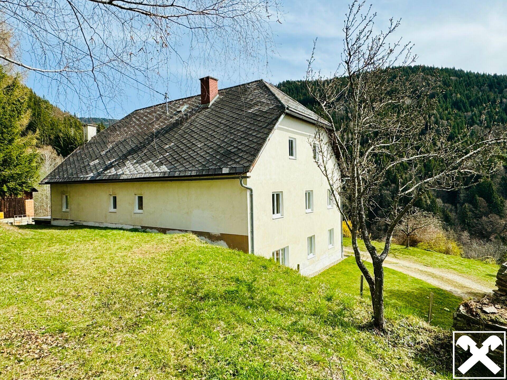 Seitenansicht des Wohnhauses mit traditionellem Dach und umgebenden grünen Wiesen.