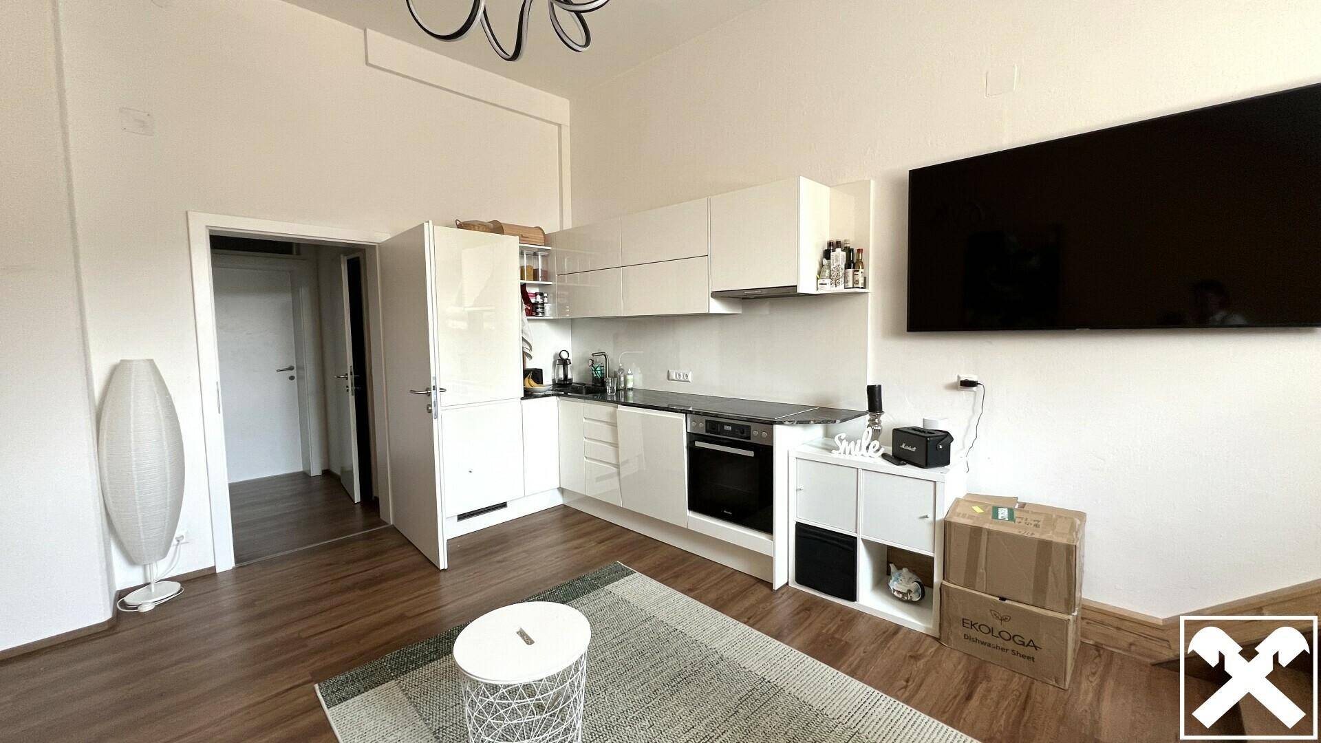 Moderne, offene Küche mit weißen Schränken, integrierten Geräten und Holzboden in einem hellen Raum.