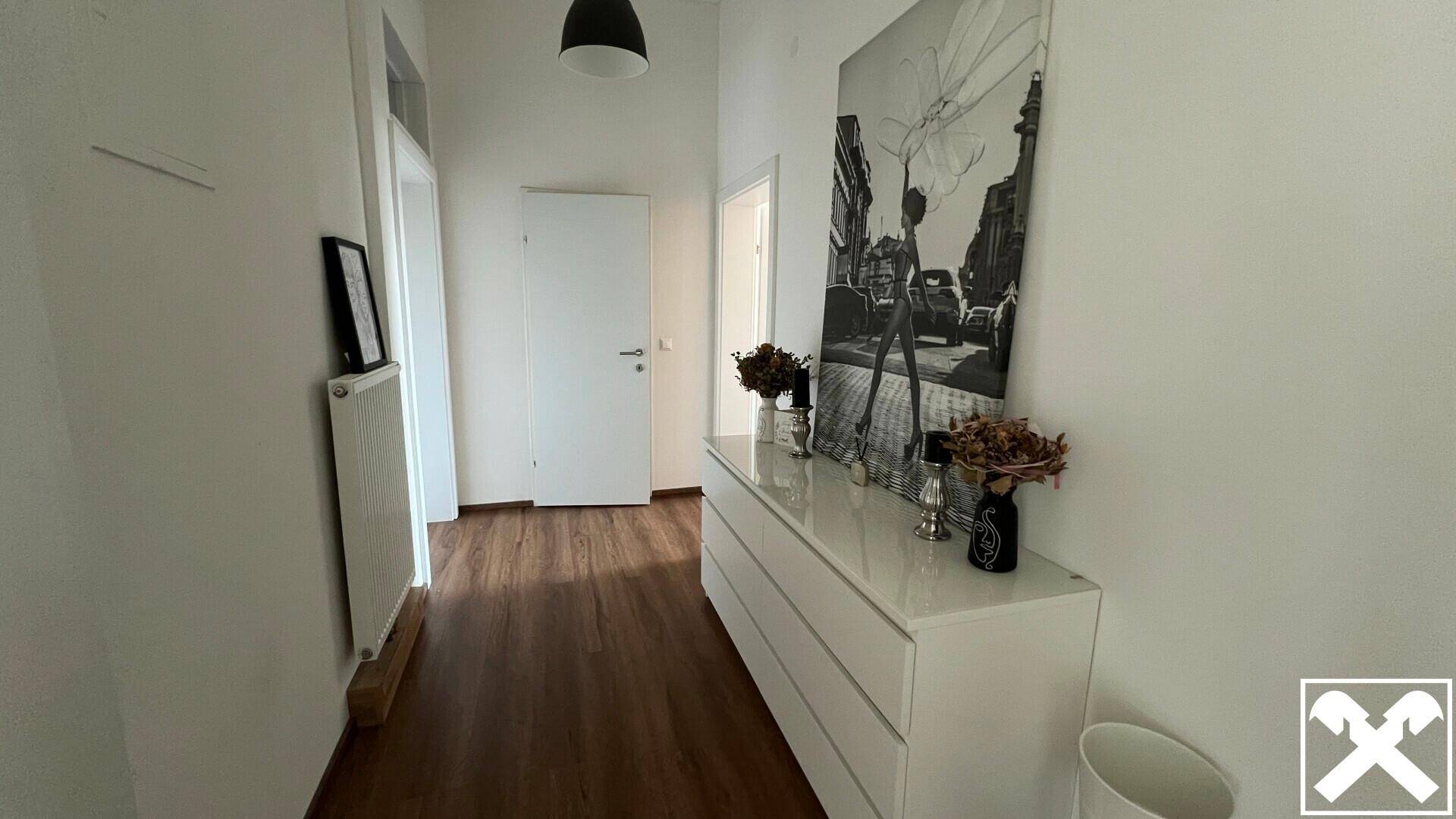 Heller Flur mit Holzboden, einer weißen Kommode und einem großen Schwarz-Weiß-Bild an der Wand.