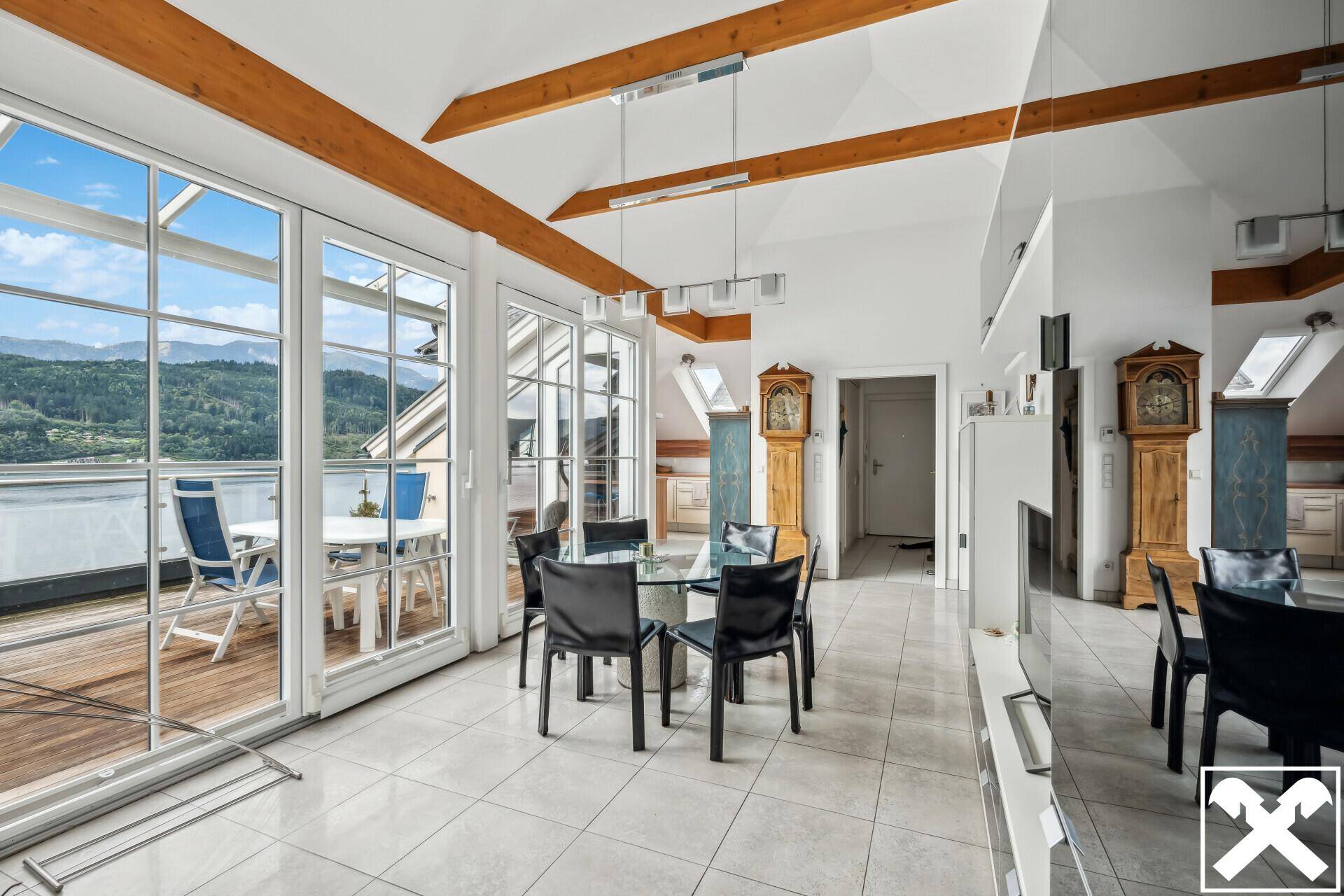 Heller Wohn-Essbereich mit Fliesenboden, Holzbalken und Zugang zu einer großen Terrasse mit Seeblick.