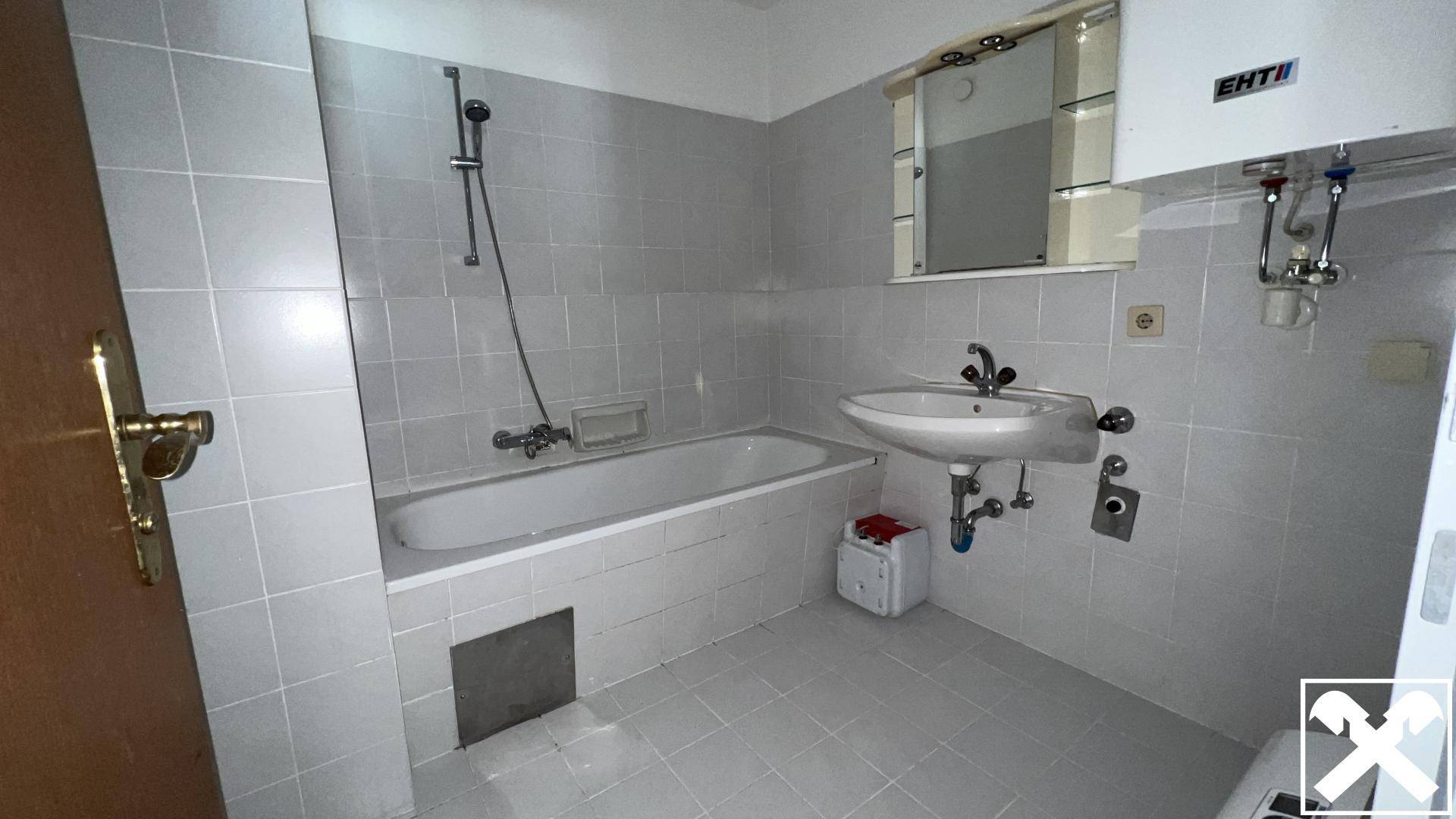 Helles Badezimmer mit hellgrauen Fliesen, einer Badewanne und einem Waschbecken mit Spiegelschrank.