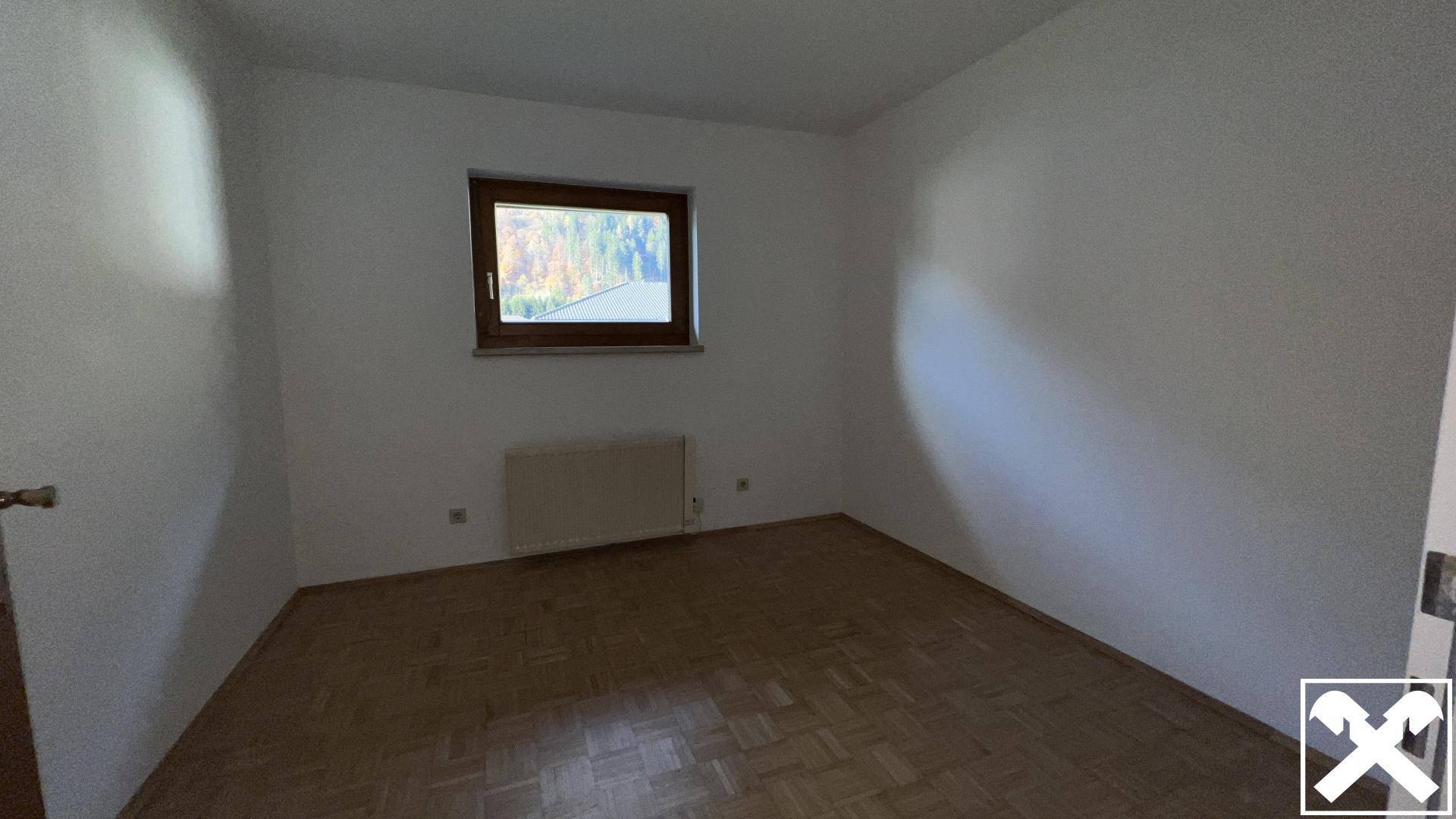 Leeres Zimmer mit Parkettboden und einem Fenster, das viel natürliches Licht hereinlässt.