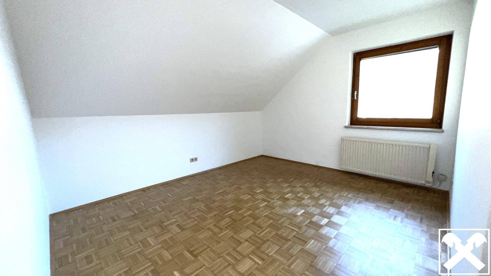 Helles Schlafzimmer im Dachgeschoss mit schrägen Wänden, Parkettboden und einem Fenster.
