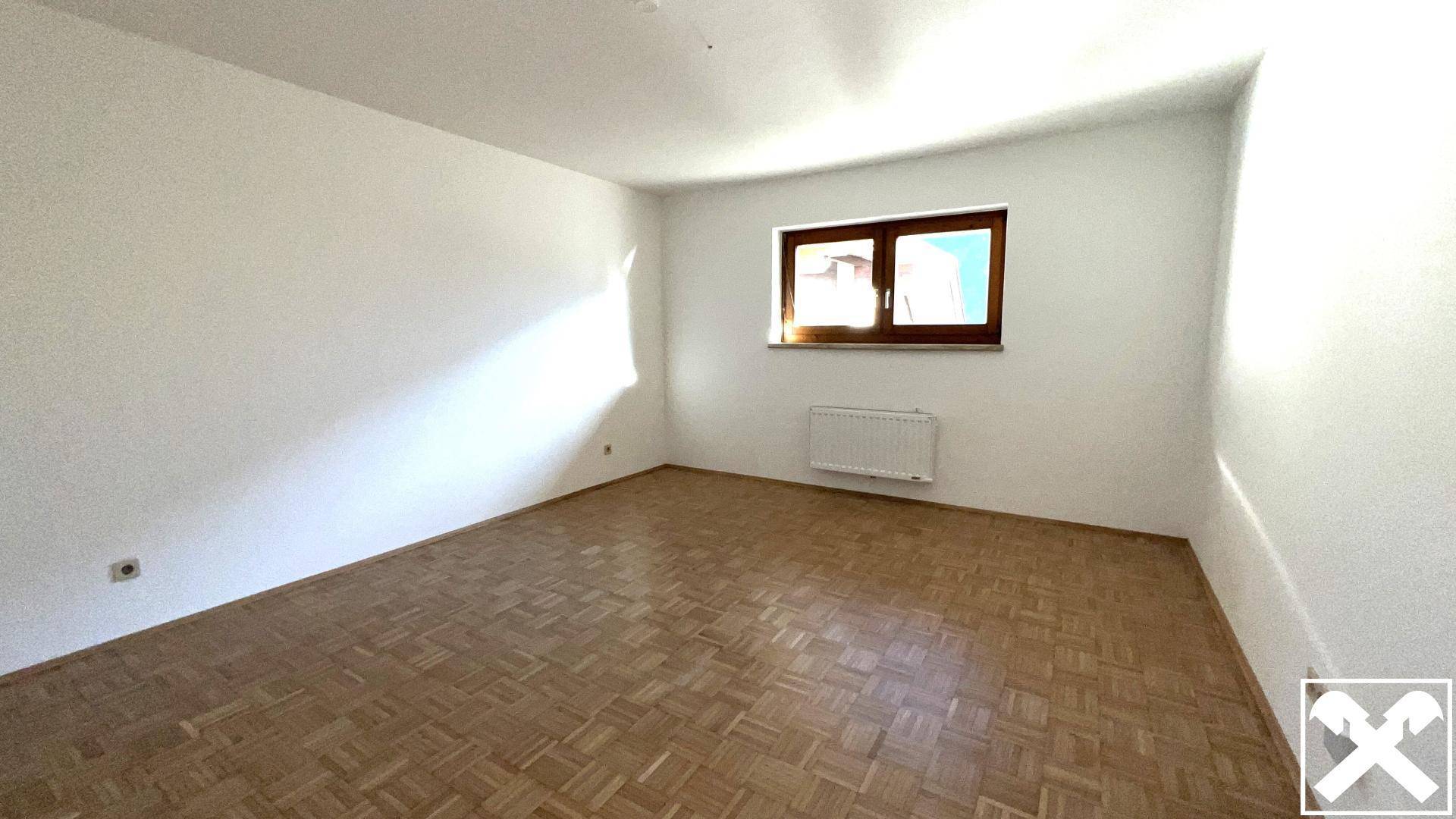Leeres Zimmer mit hellem Parkettboden und einem Fenster, das für gute Belichtung sorgt.