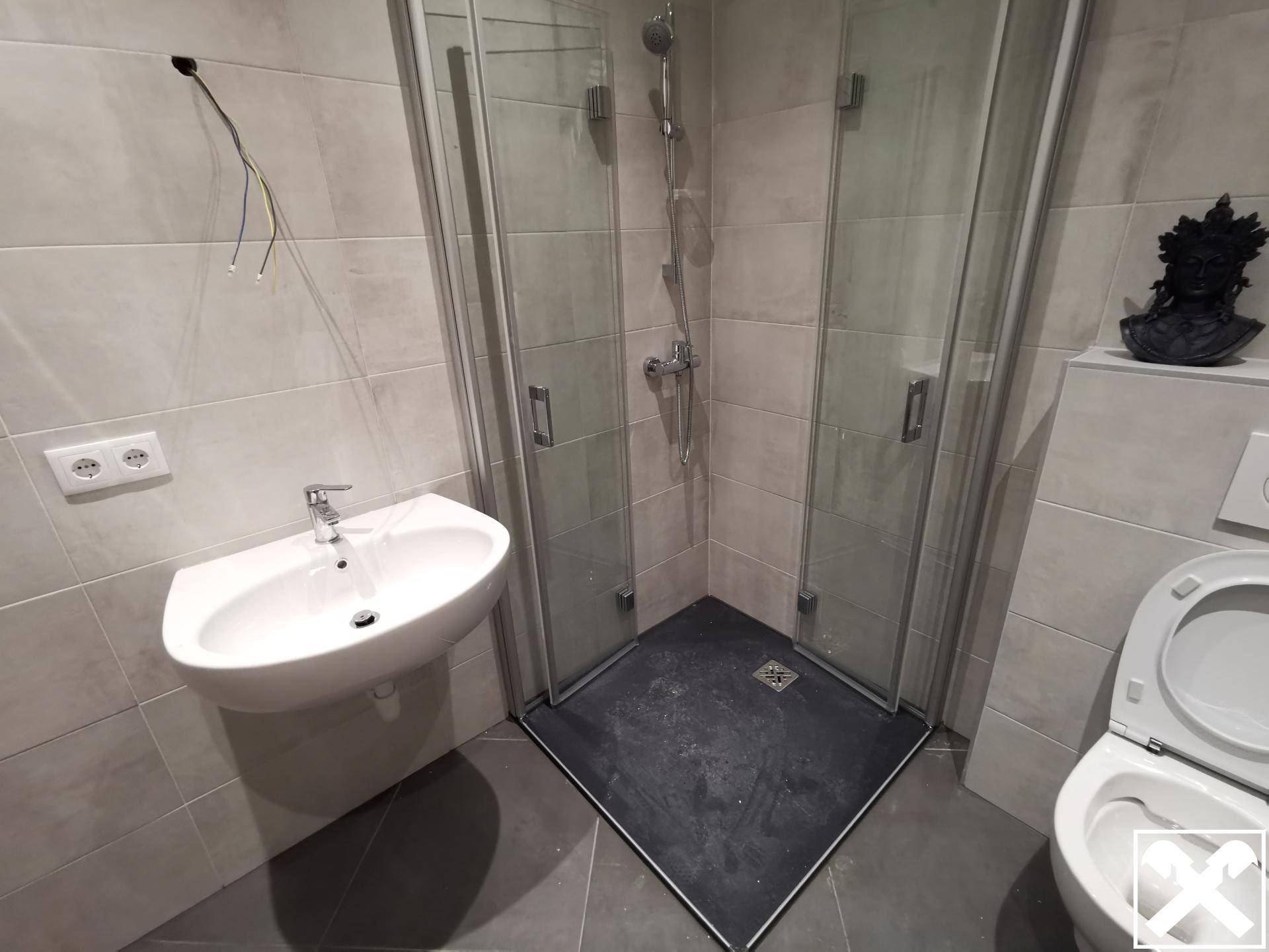 Modernes Badezimmer mit Dusche, Waschbecken und WC, gefliest in neutralen Farbtönen.