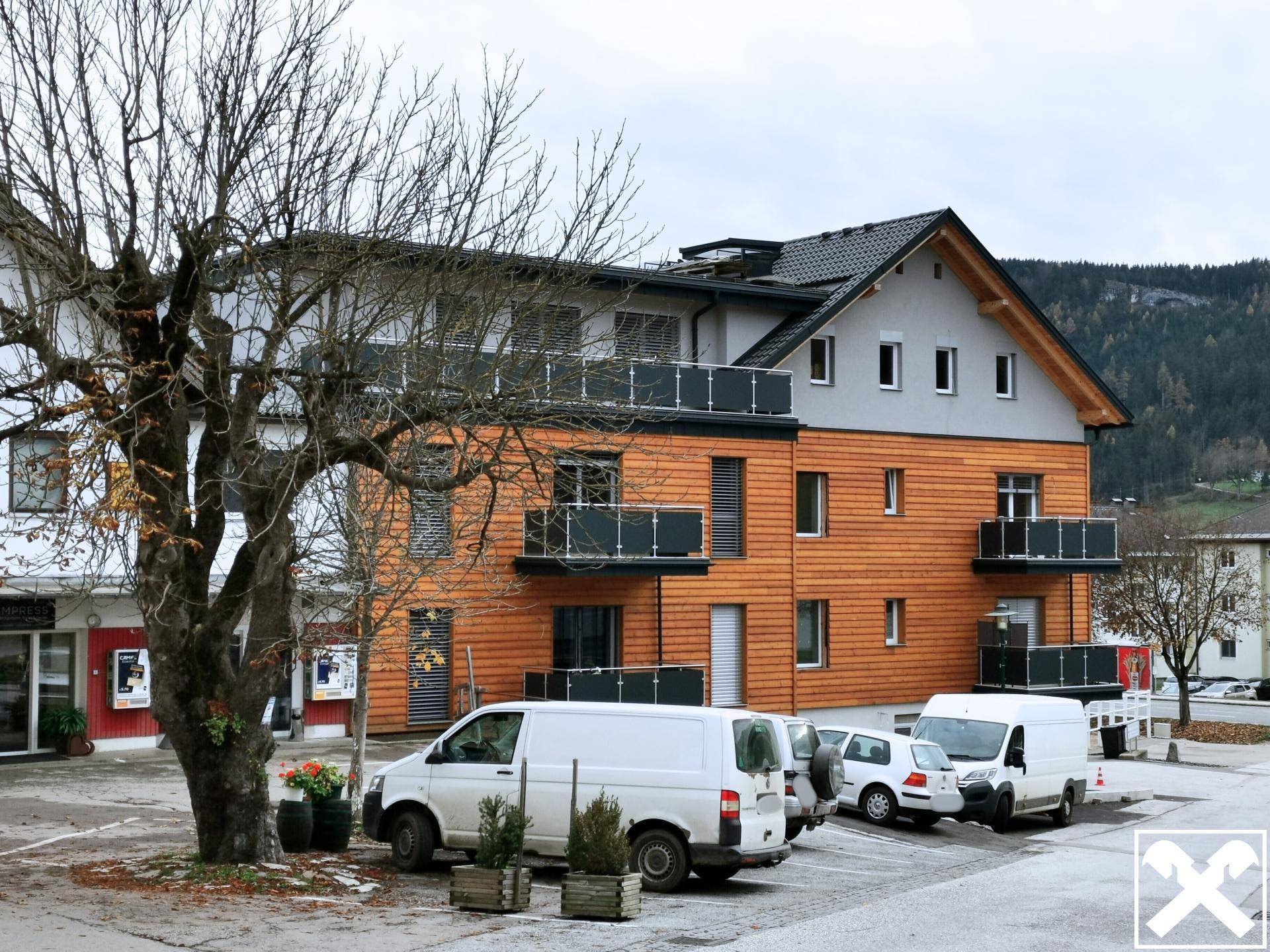 Neubau mit Holzfassade, Balkonen und Parkplätzen im ländlichen Umfeld.