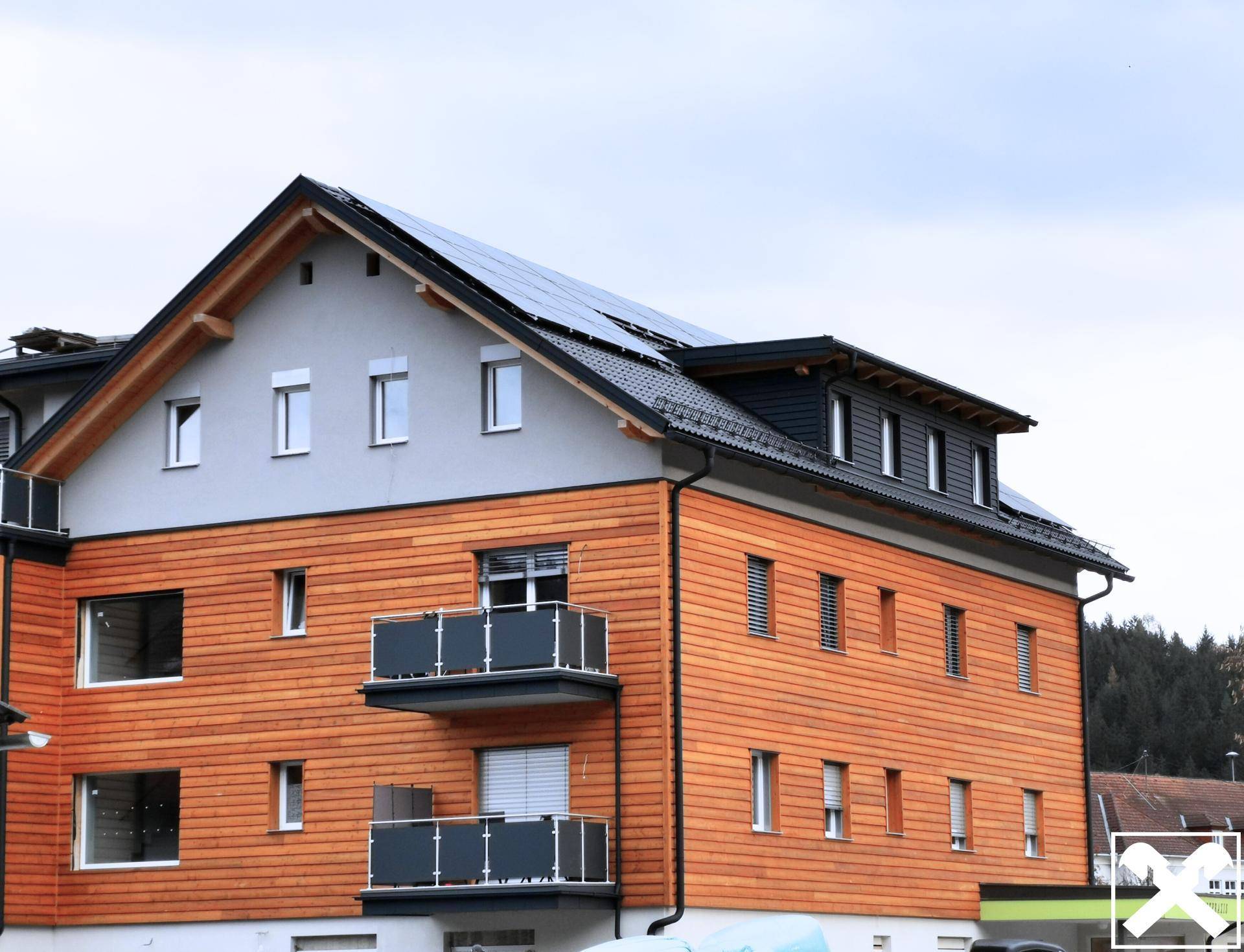 Detailansicht der modernen Holzfassade mit Balkonen und Solarpaneelen auf dem Dach.