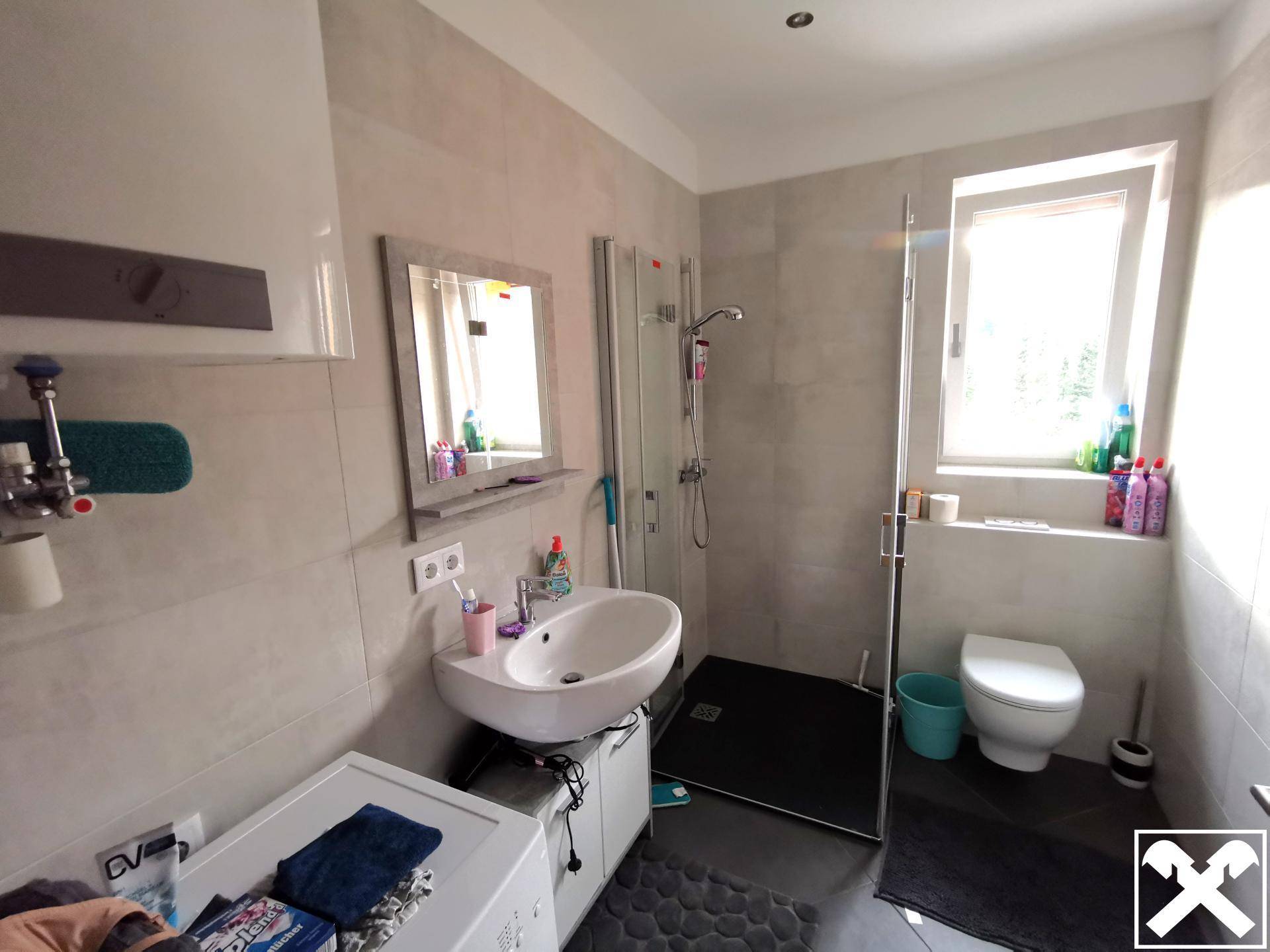 Helles Badezimmer mit Dusche, Waschbecken, WC und Fenster, ausgestattet mit Waschmaschine.