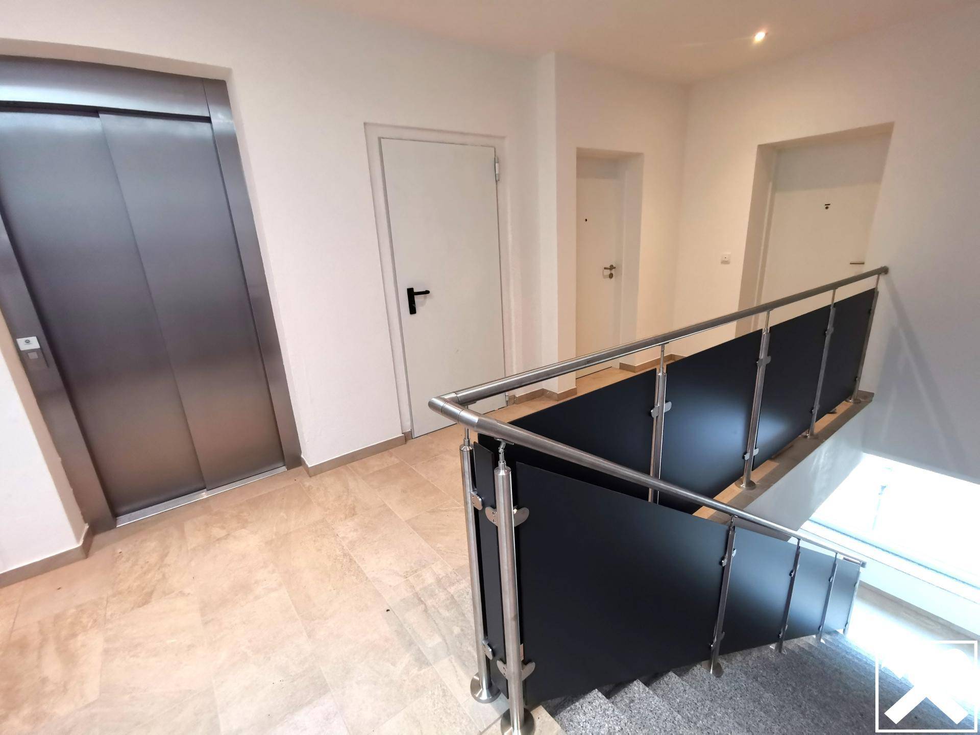 Heller Flur mit Aufzug und Treppenhaus, ausgestattet mit modernen Geländern.