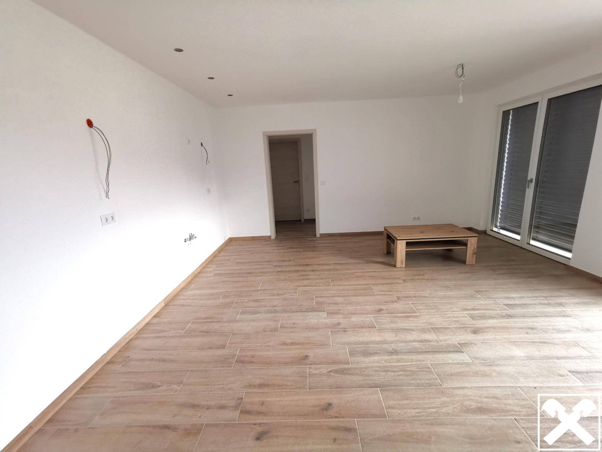 Geräumiger, heller Wohnbereich mit Holzoptikfliesen und großen Fenstern.
