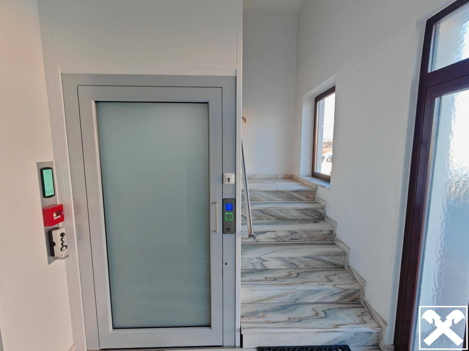 Heller Eingangsbereich mit Marmortreppe und modernem Aufzug für barrierefreien Zugang.