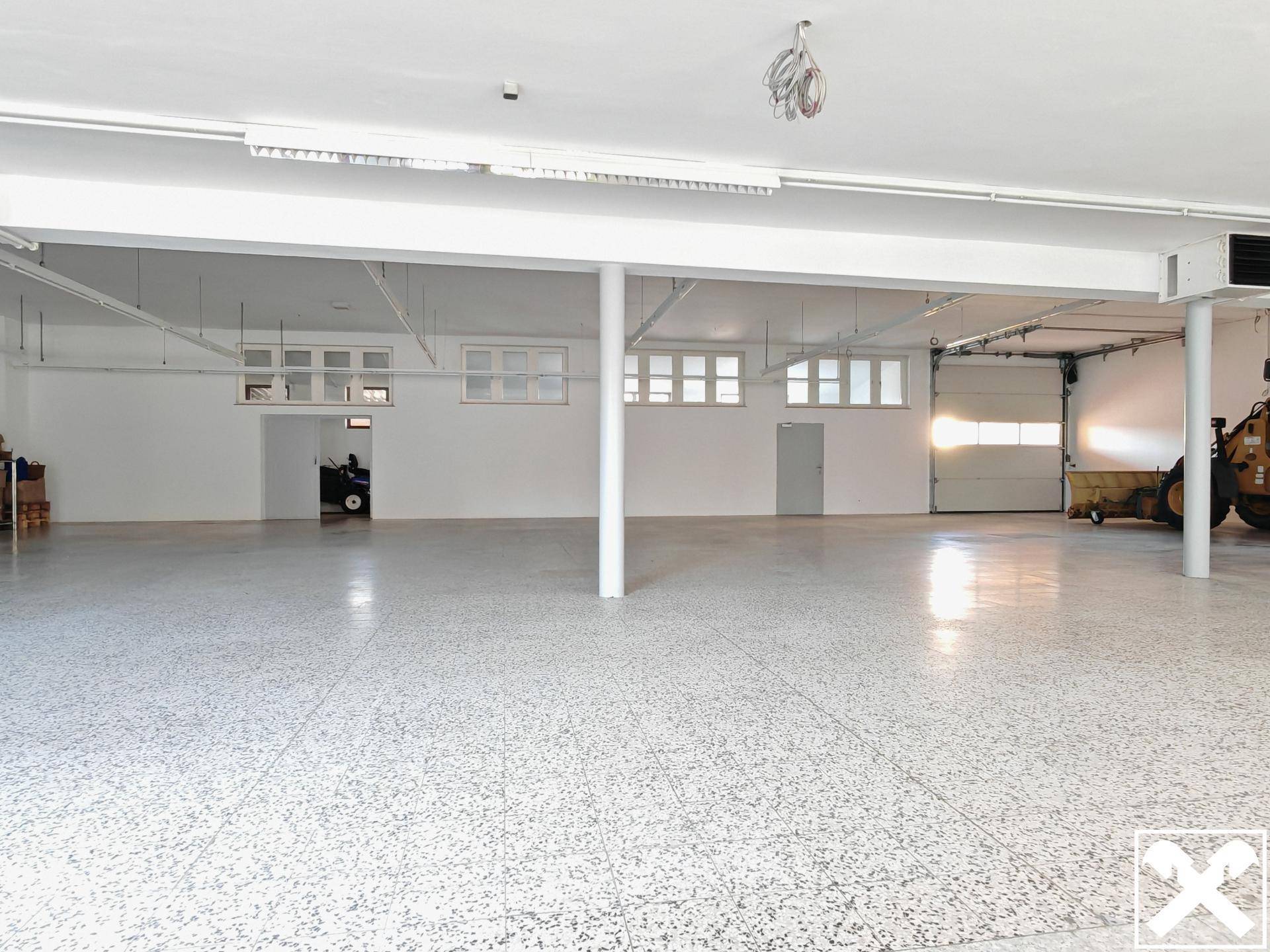Geräumige Lagerhalle mit hohen Decken, Terrazzoboden und großem Rolltor für bequemen Fahrzeugzugang.